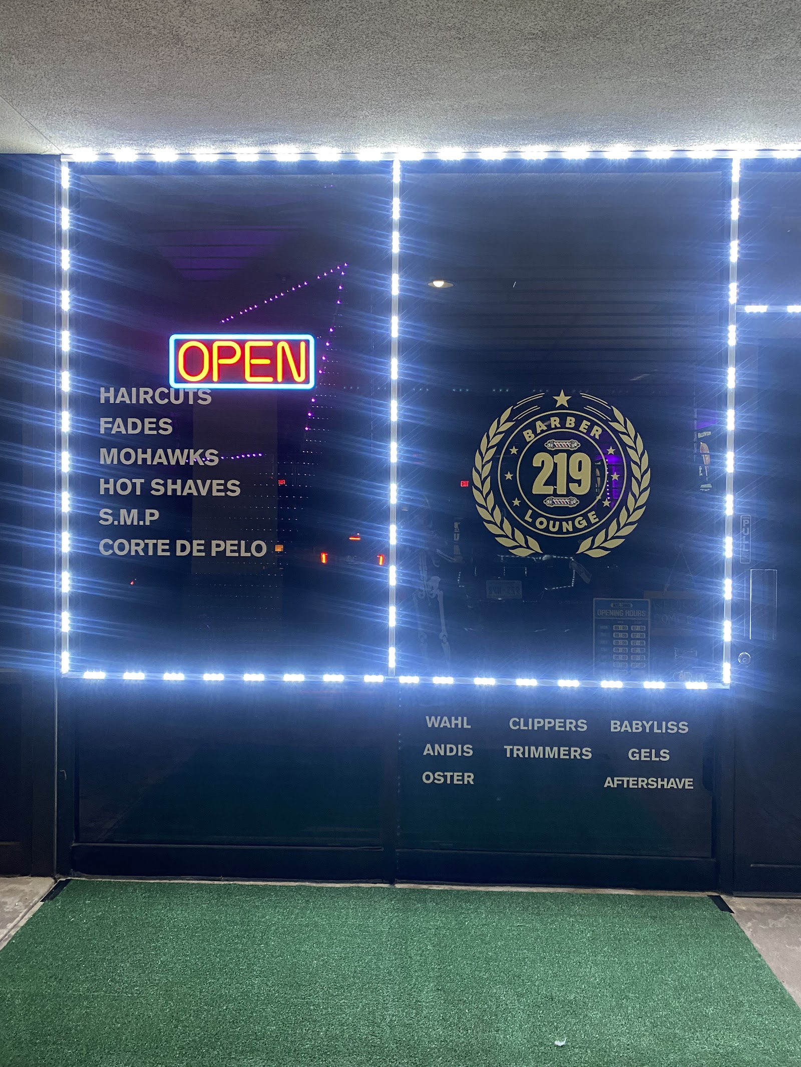 Storefront window at night with OPEN neon sign and service list