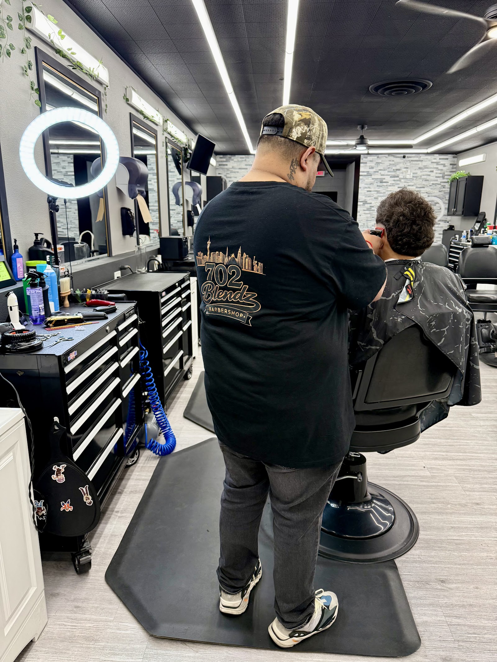 Barber wearing 702 Blendz shirt cutting a young client's hair inside the shop