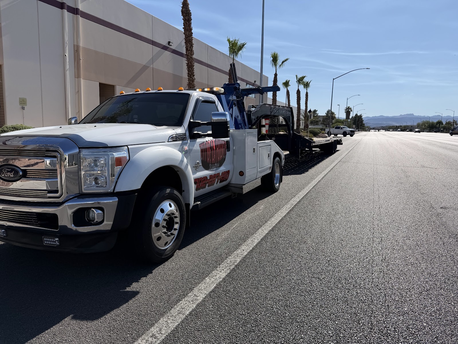 White Ford F-450 wrecker tow truck with flatbed trailer on a wide road