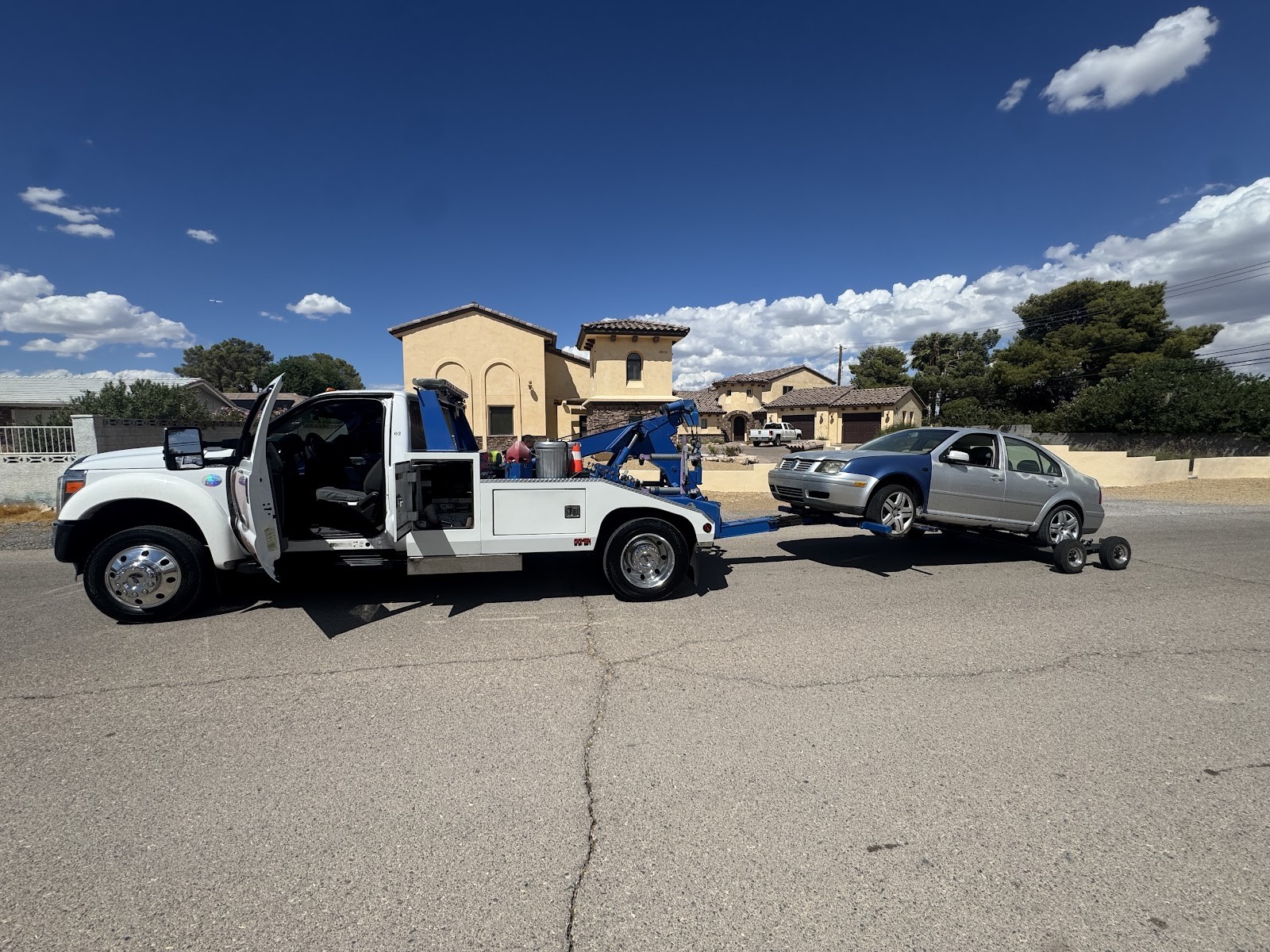 Ford tow truck wheel-lift towing a silver VW Jetta in a residential neighborhood