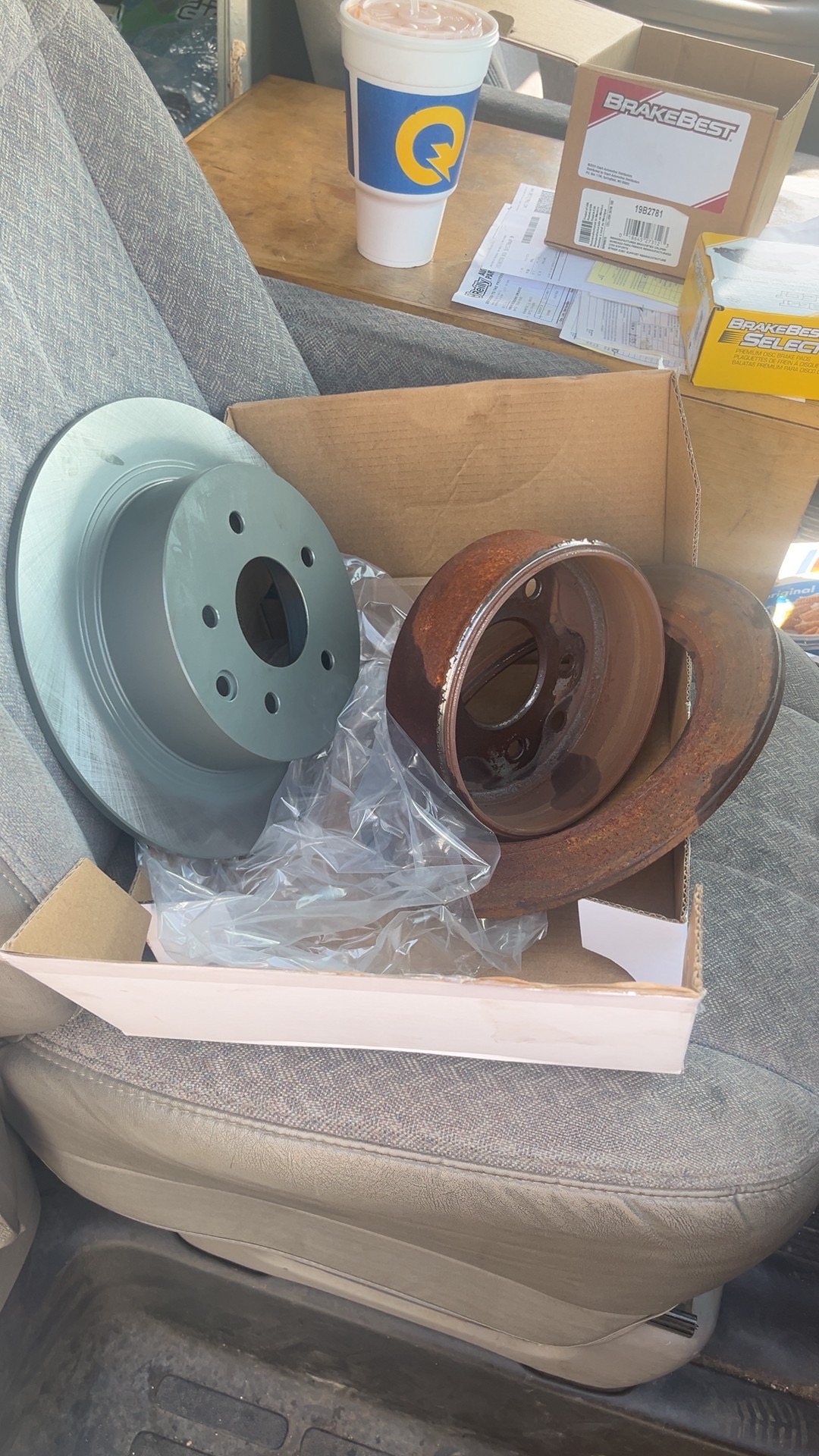 New brake rotor beside rusty old rotors in a box on a vehicle seat