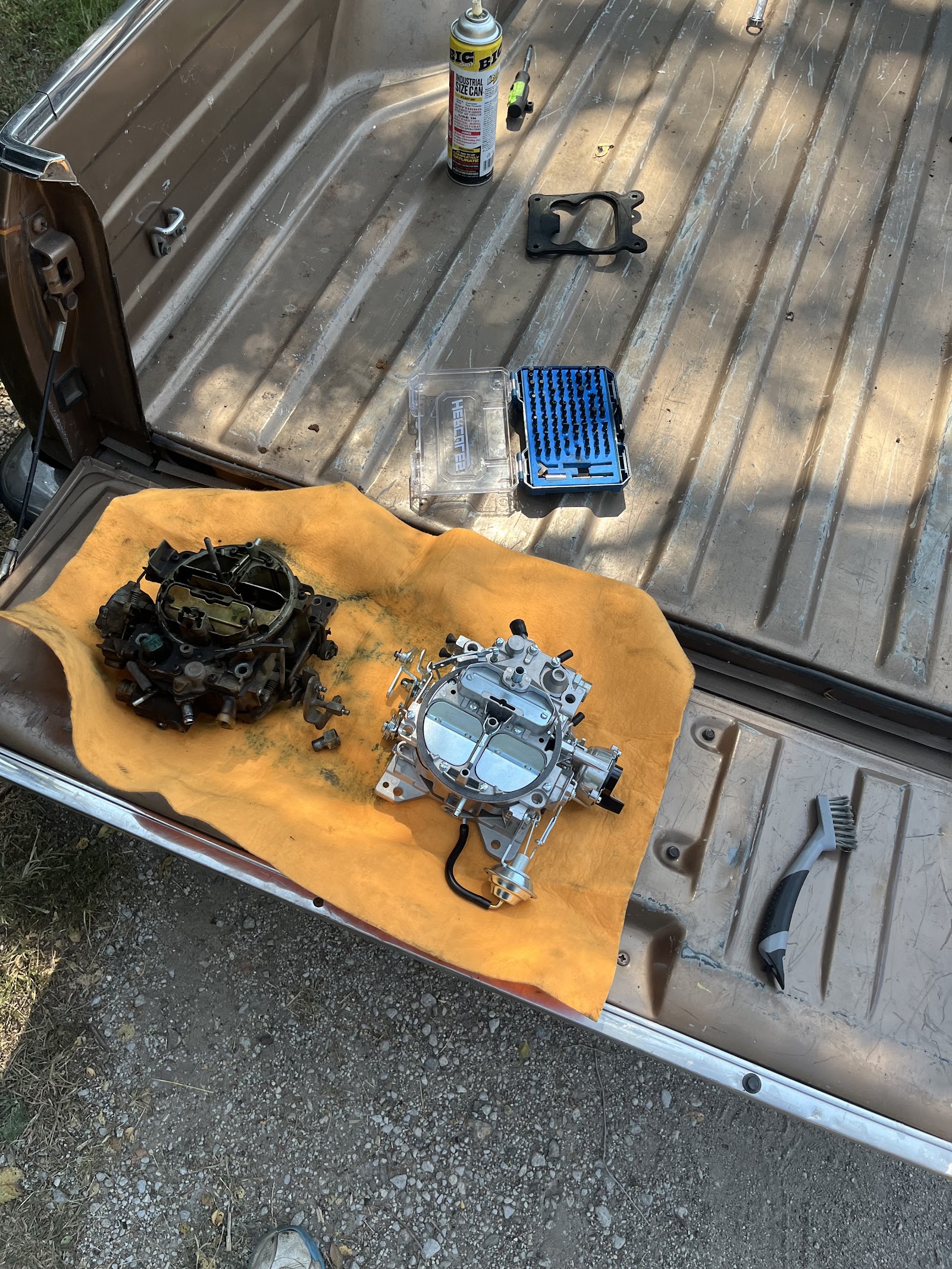 Old and rebuilt carburetors laid out on a truck tailgate with tools