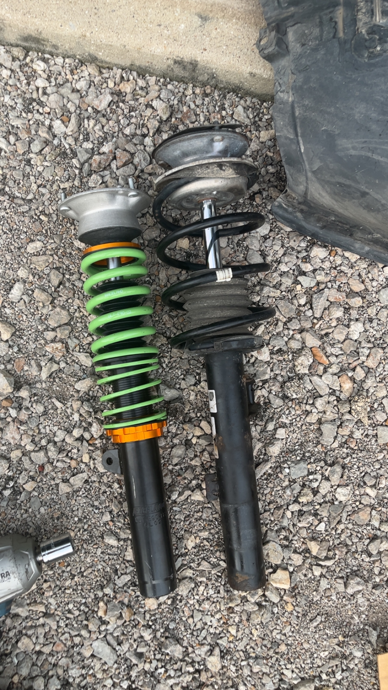 New green Raceland coilover next to worn OEM strut assembly on gravel