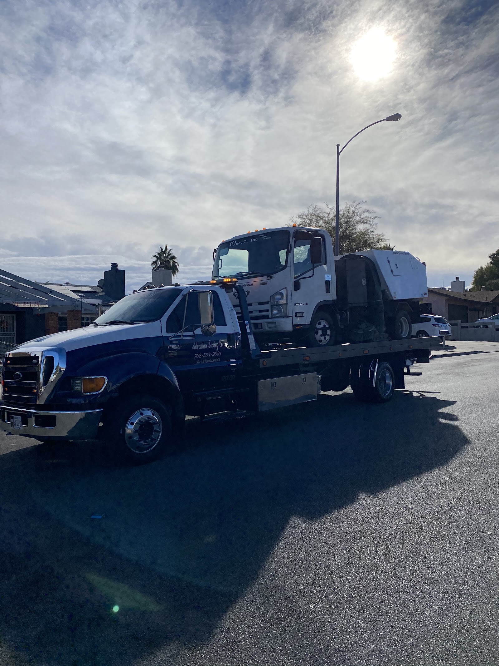 Adventure Towing Co. flatbed carrying a box truck, phone 702-533-9691 on door