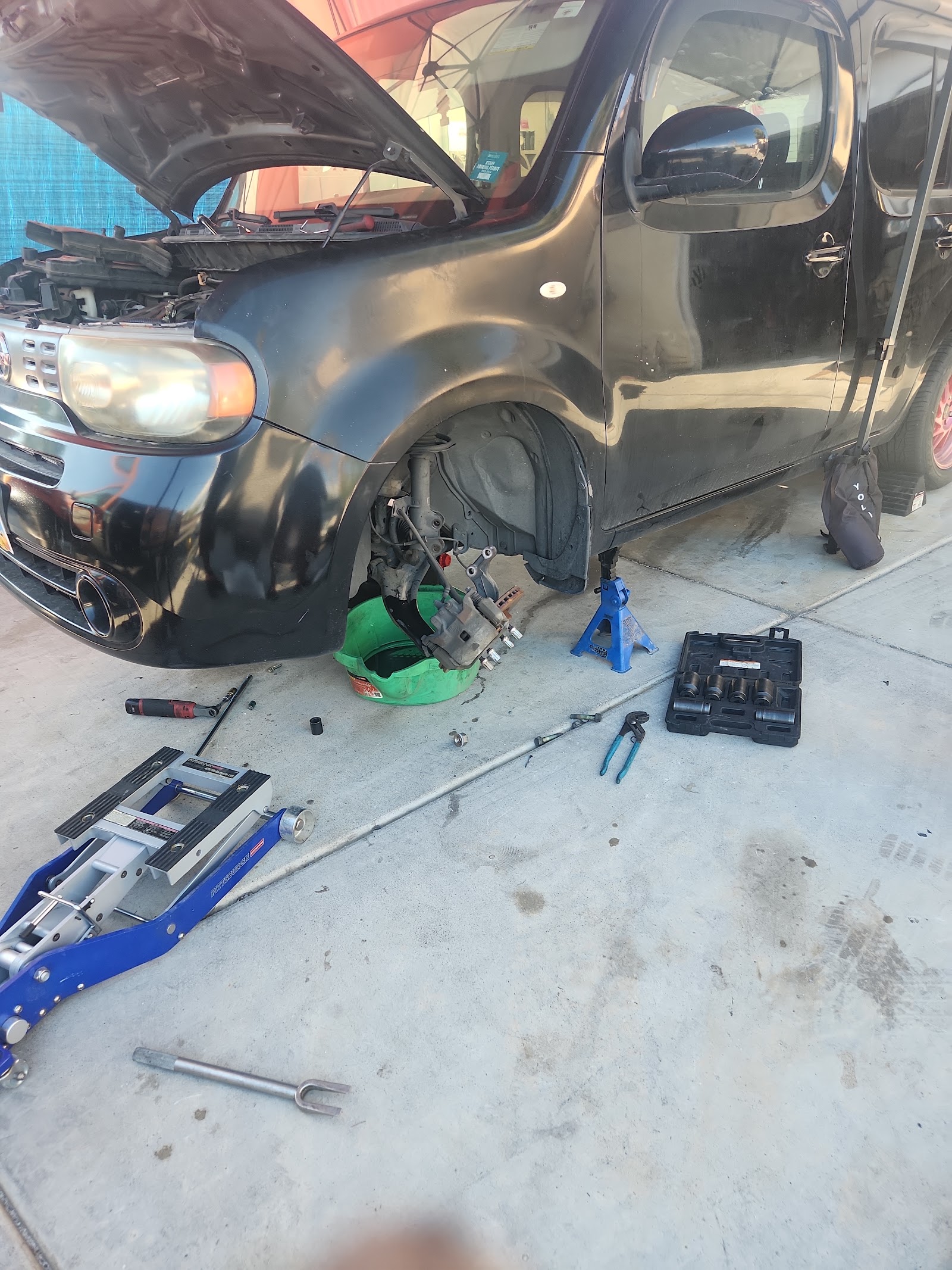 Black Nissan Cube on jack stands with brake components and tools during repair