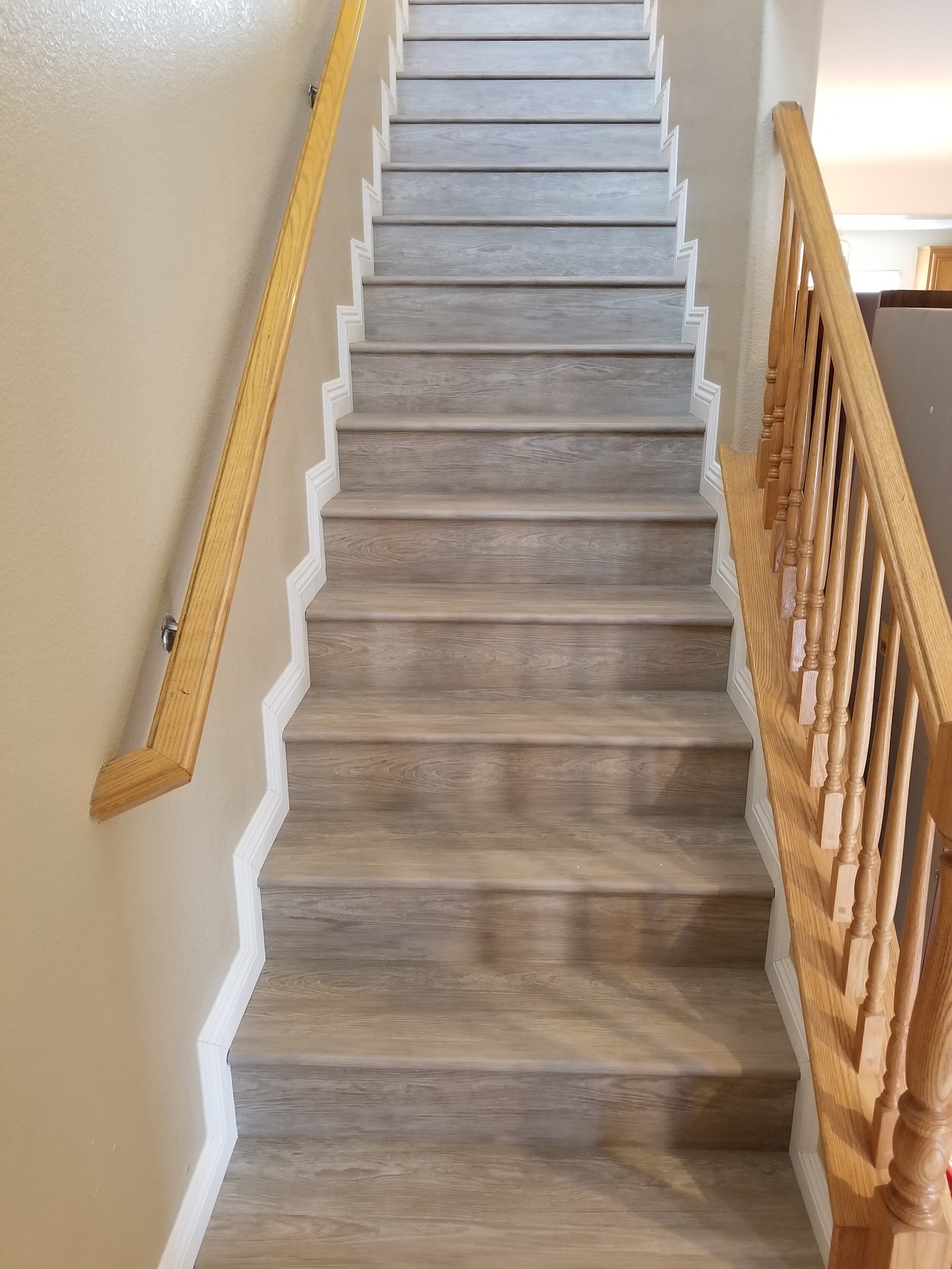 Interior staircase with gray wood-look plank treads, white risers and oak railing