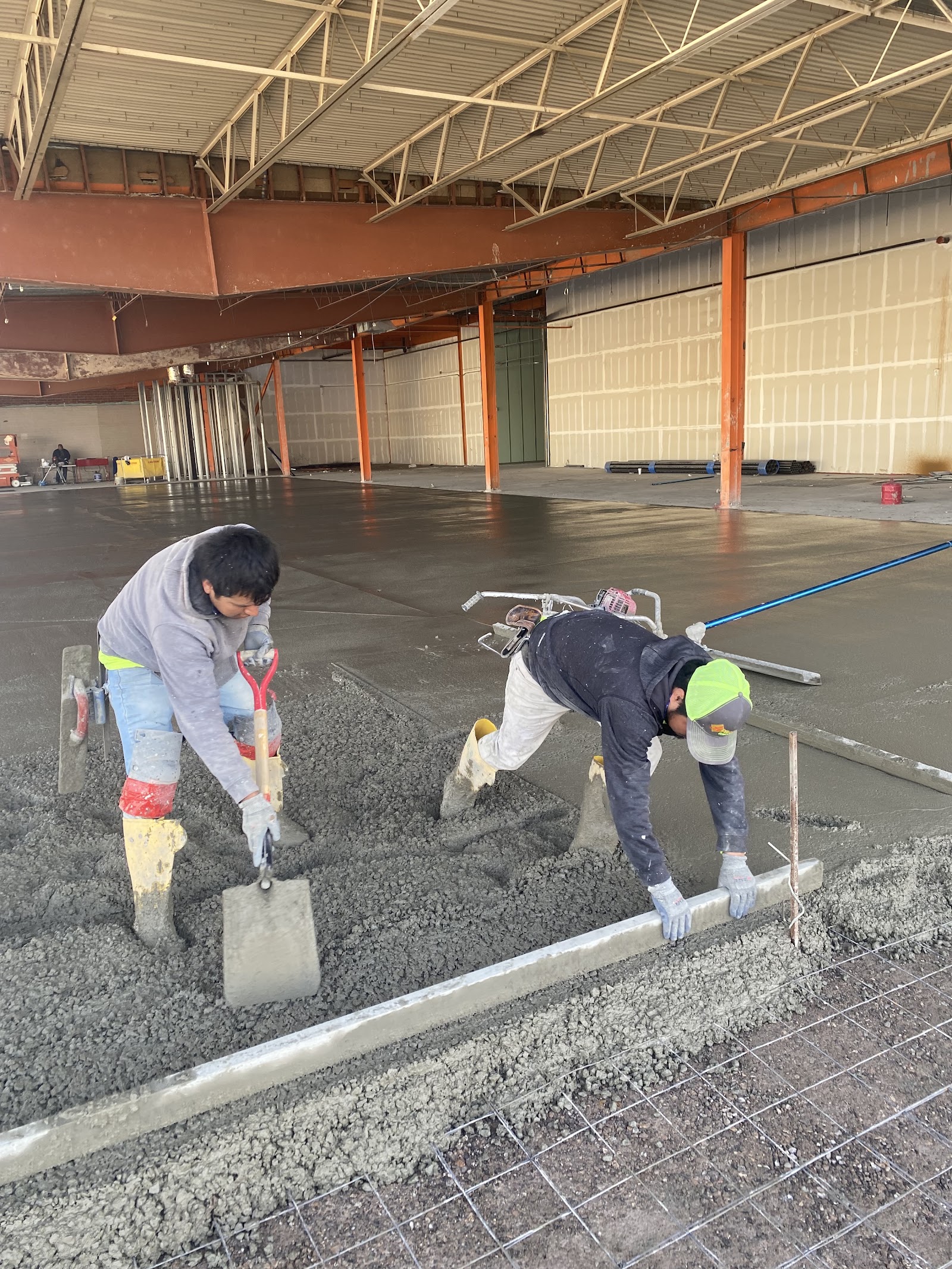 Two workers finishing a large interior concrete slab pour
