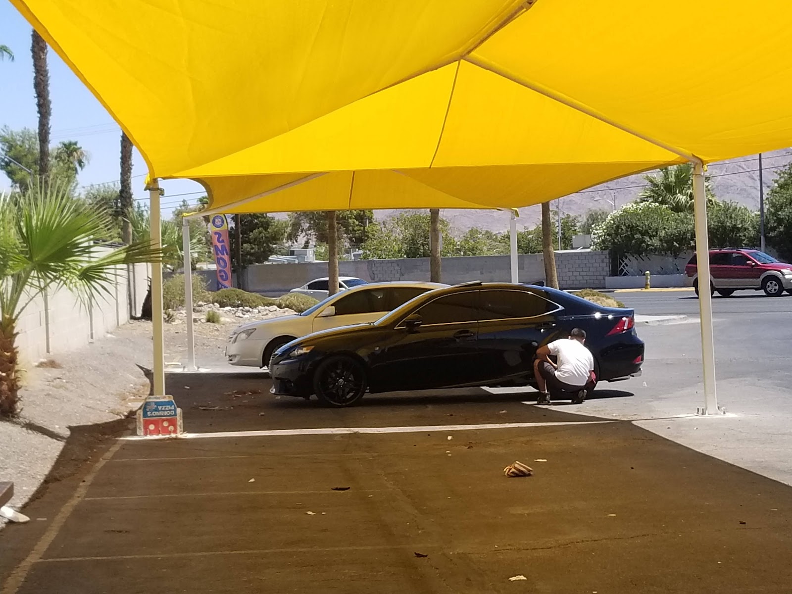 Worker hand-drying a black Lexus under yellow shade canopy