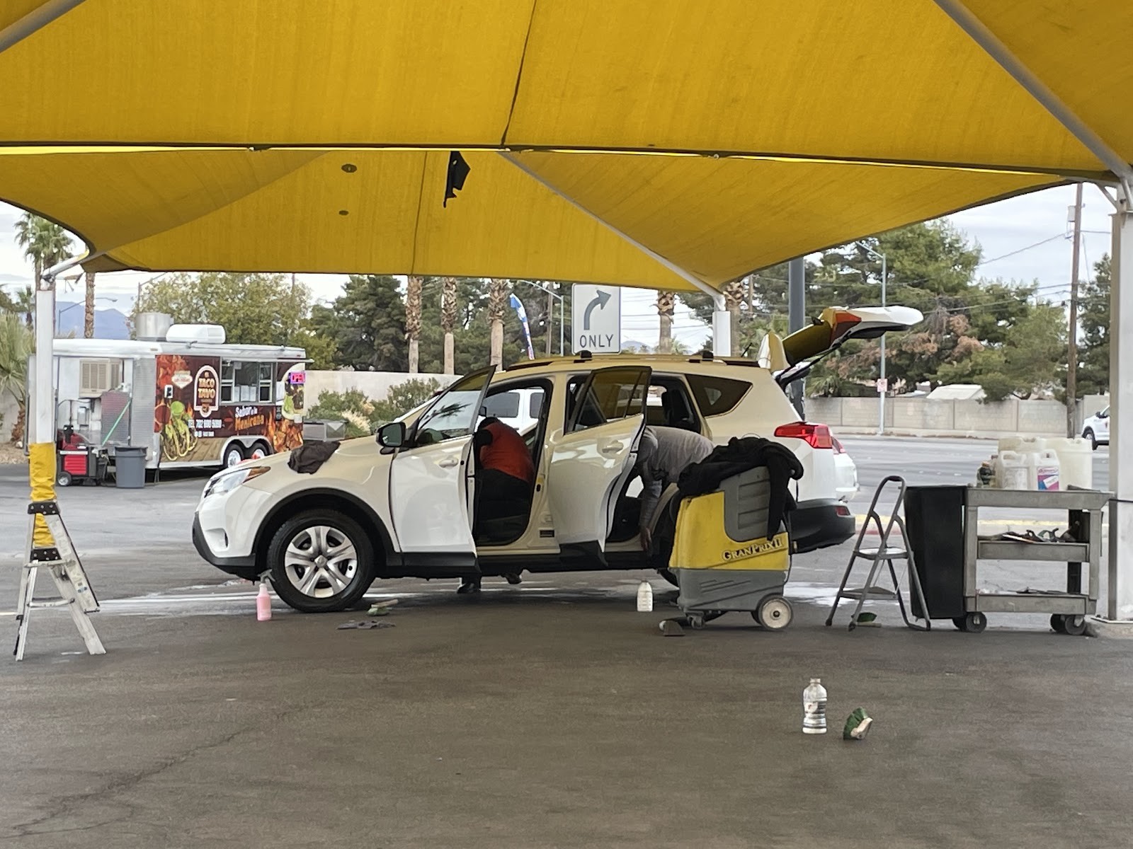 Two workers detailing a white SUV with extractor under shade canopy