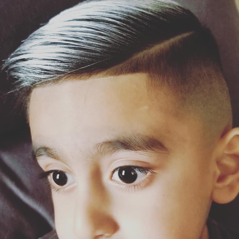 Young boy with slicked comb-over fade and hard part design