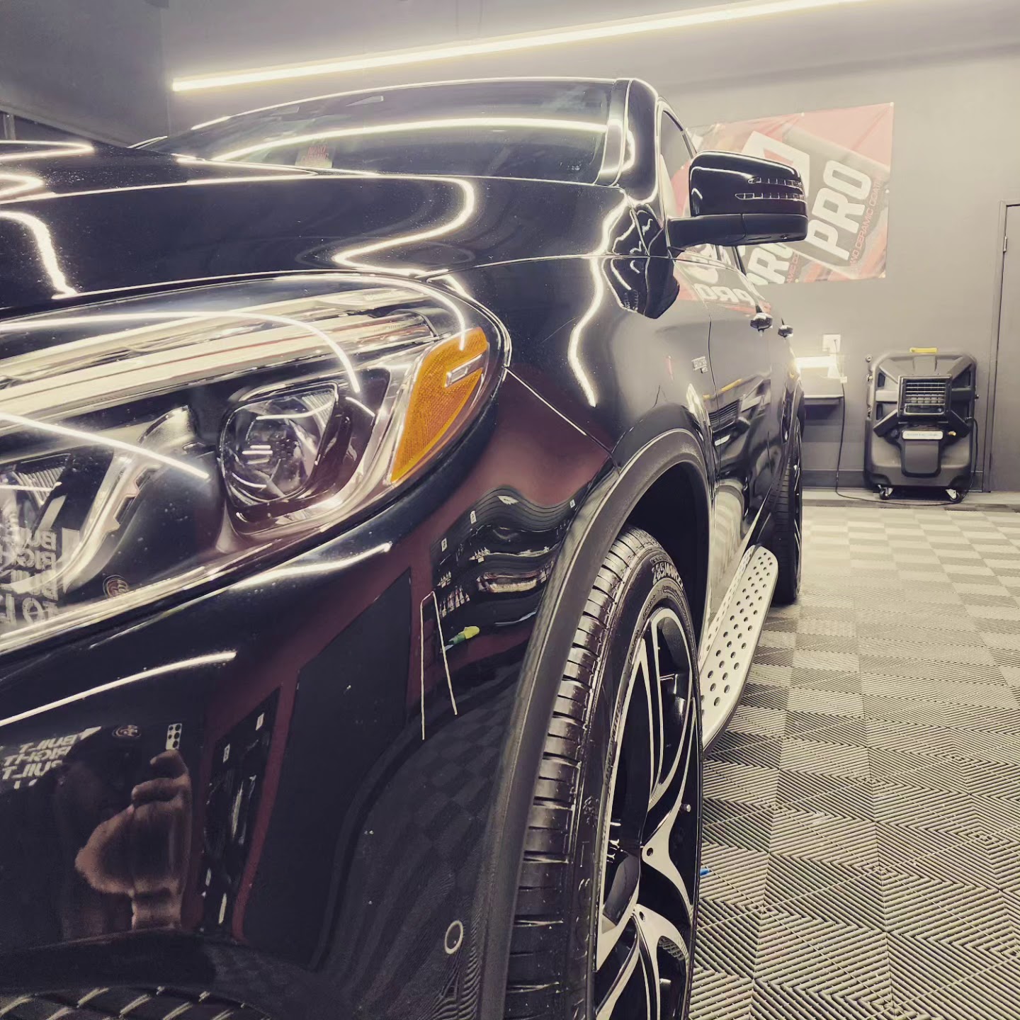 Front headlight and fender of a black Mercedes SUV in detailing shop