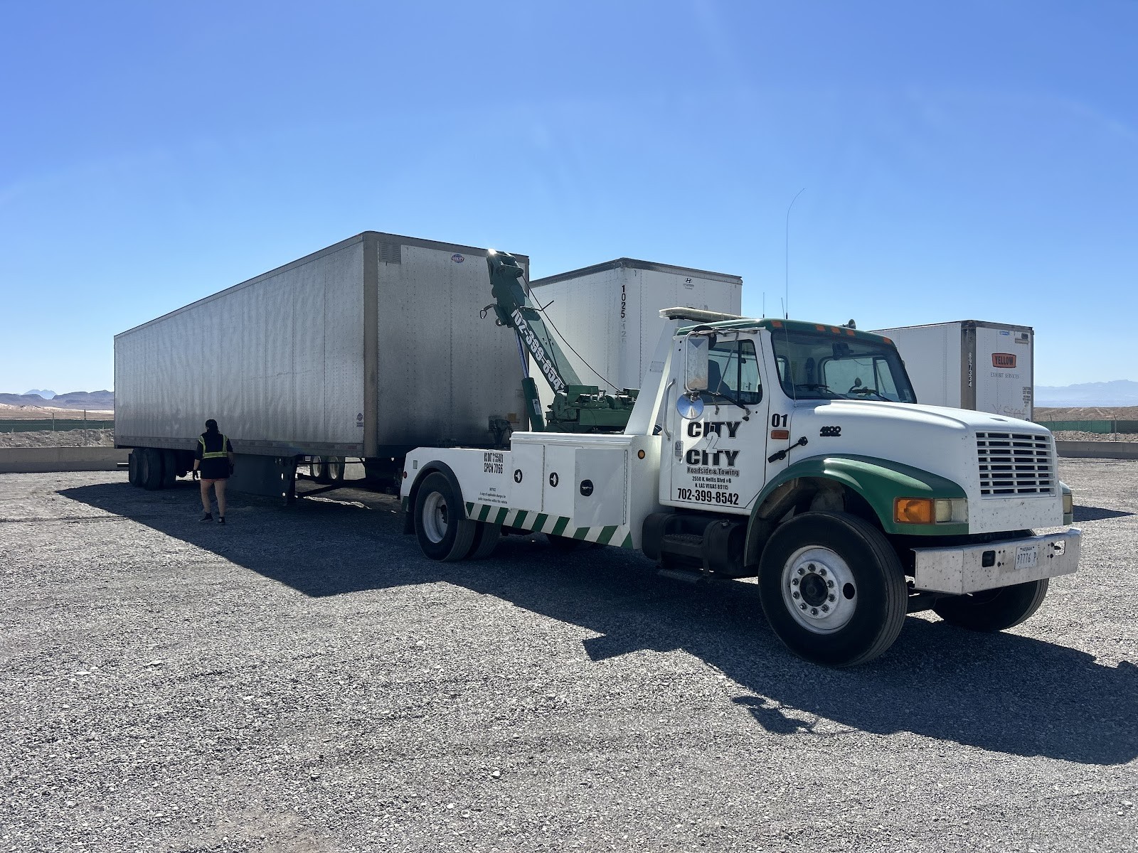 City 2 City wrecker hooked to a semi-trailer in an open lot with worker