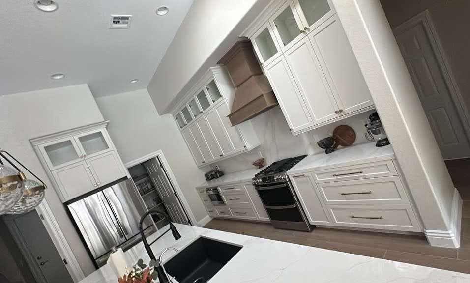 White kitchen with wood range hood, glass cabinets, and marble countertops
