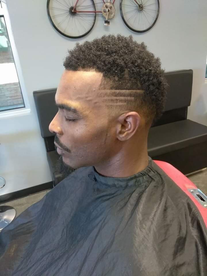 Side profile of man with curly top, fade and hair design lines