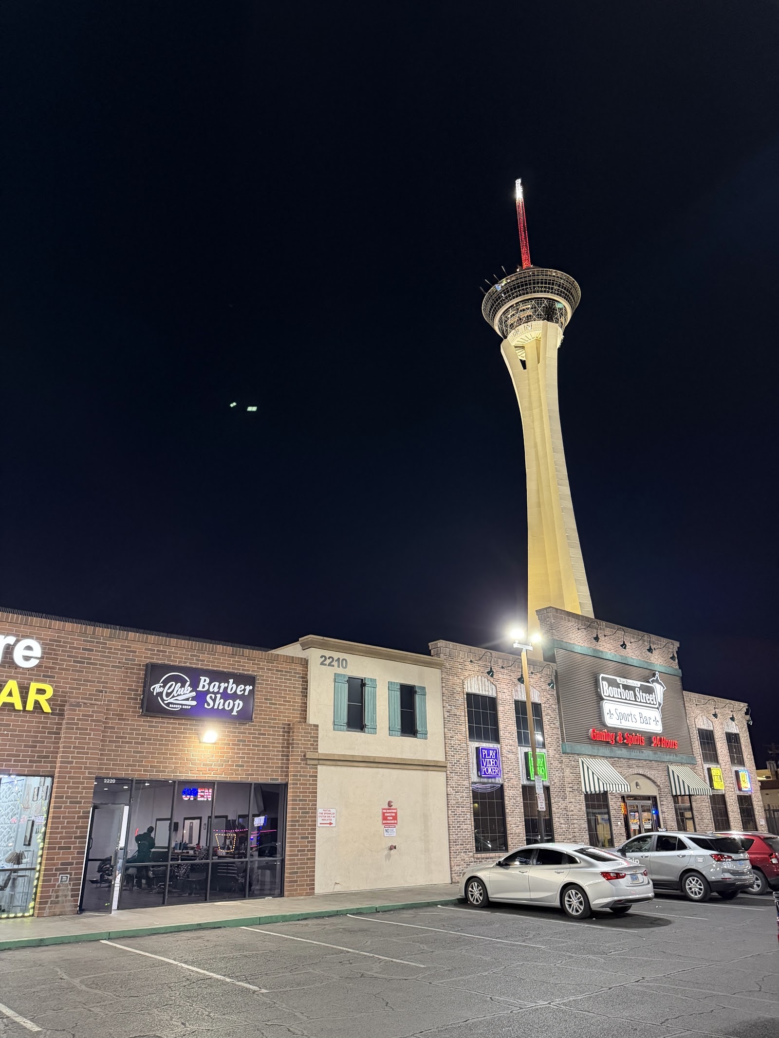 The Club Barber Shop exterior at night with the Strat tower lit in the background