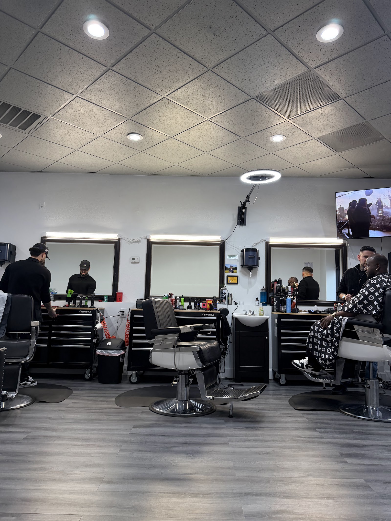 Interior of barbershop with multiple barbers working at stations, clients in chairs, TV on wall