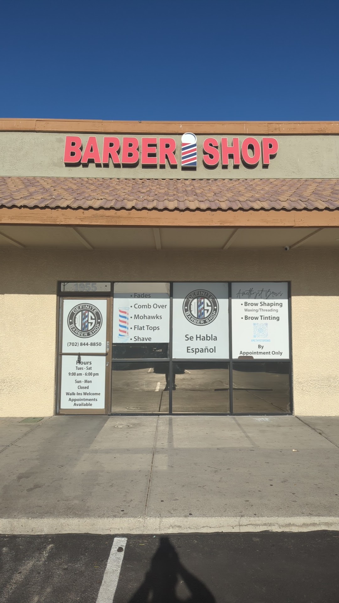 Exterior of Definite Barber Shop with red BARBER SHOP sign under blue sky