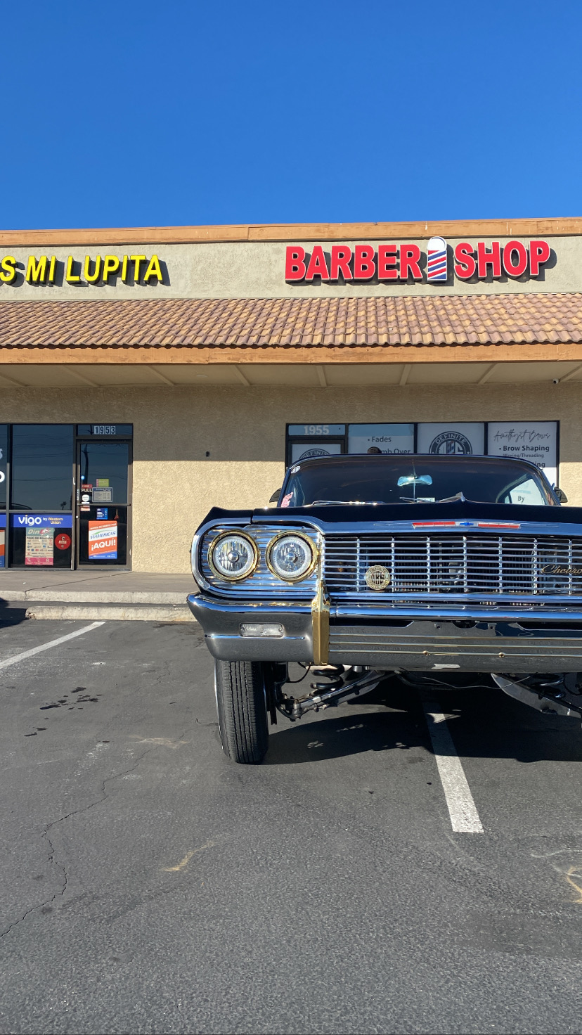 Classic black lowrider Chevrolet Impala parked outside the barbershop storefront