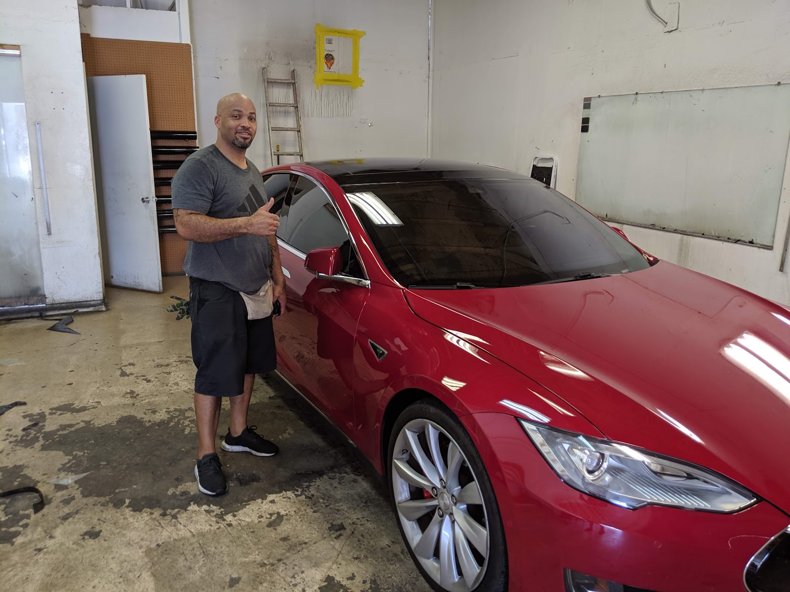 Smiling customer giving thumbs up next to a red Tesla Model S with tinted windows