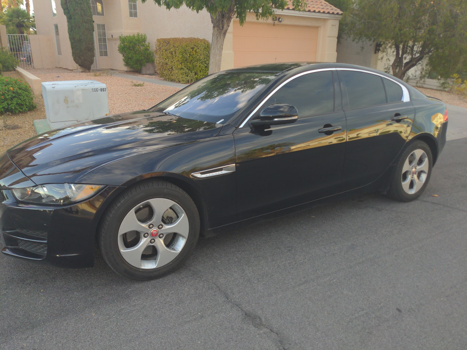 Black Jaguar sedan with tinted windows parked in a residential driveway