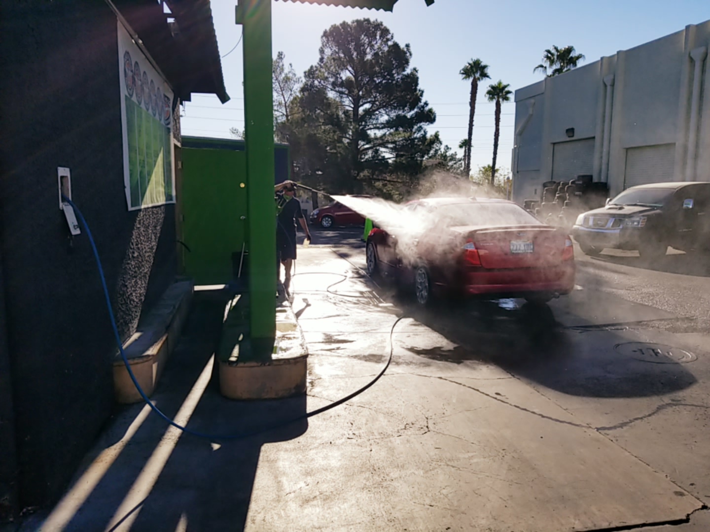 Worker pressure washing a red sedan at the wash bay