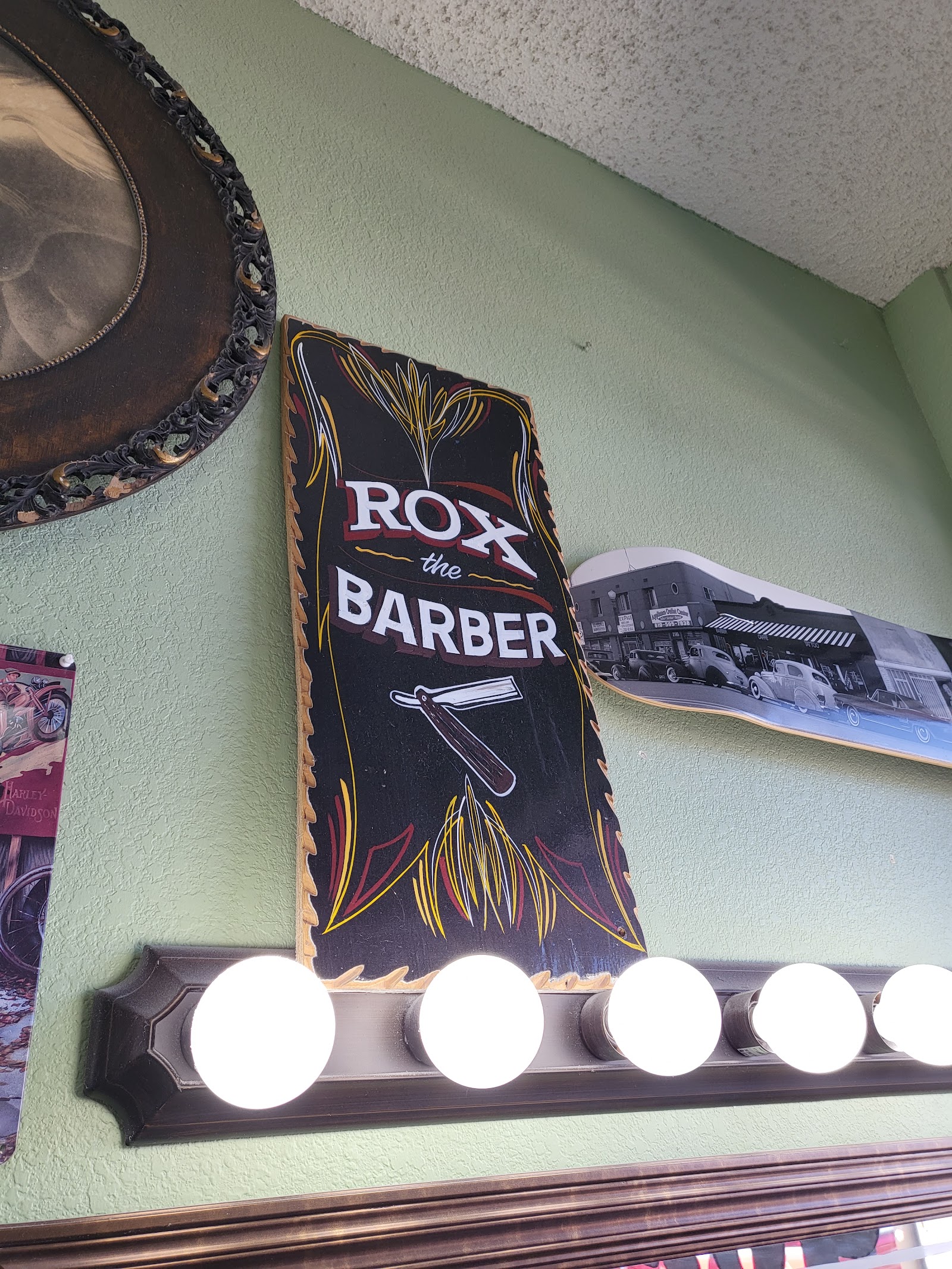 Hand-painted 'Rox the Barber' pinstriped sign on green wall above vanity lights