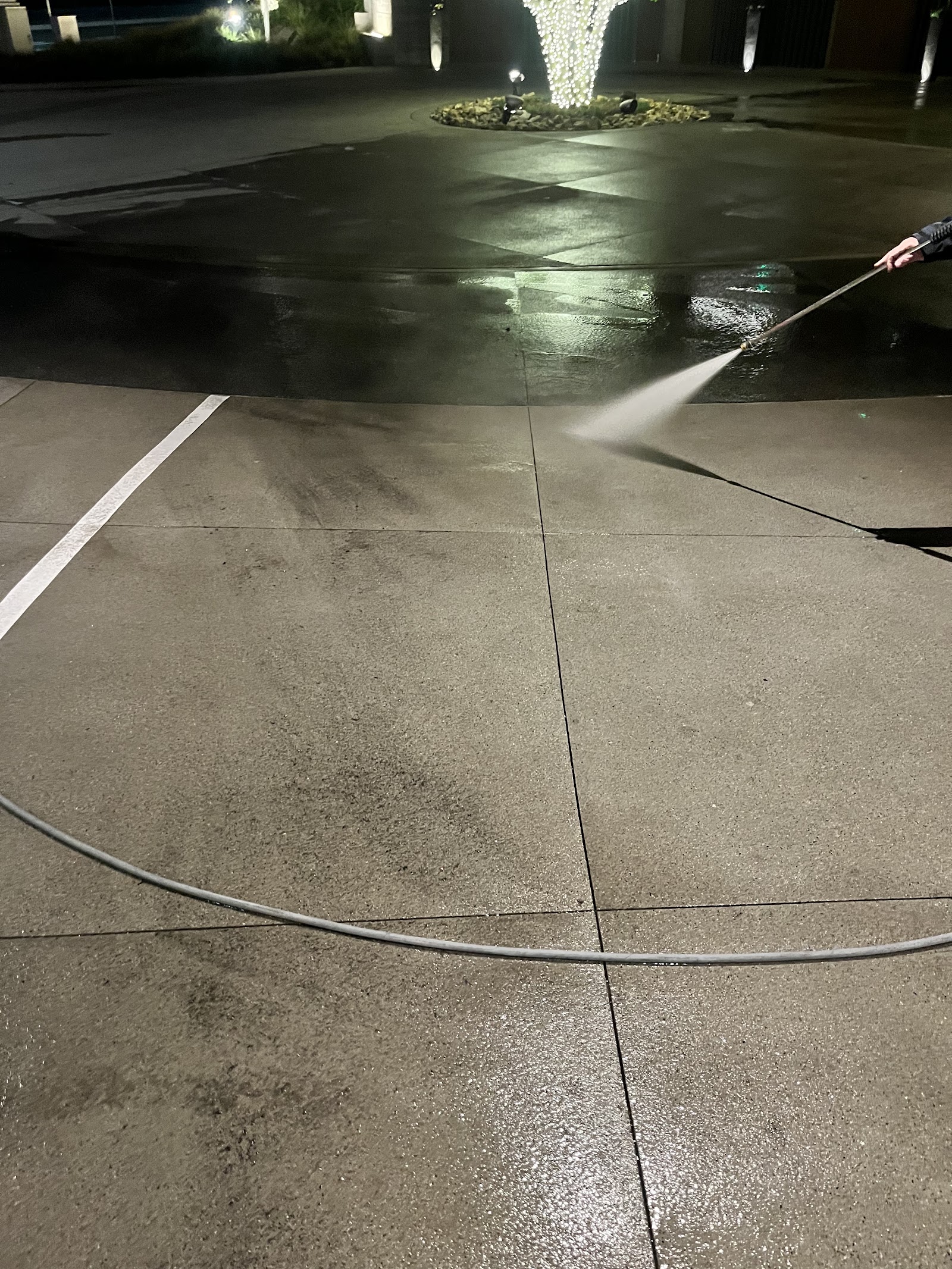 Worker pressure washing commercial concrete at night