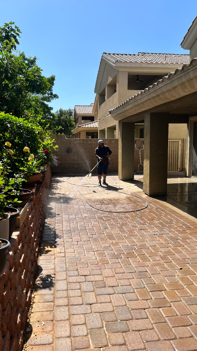 Worker pressure washing paver walkway between homes on a sunny day
