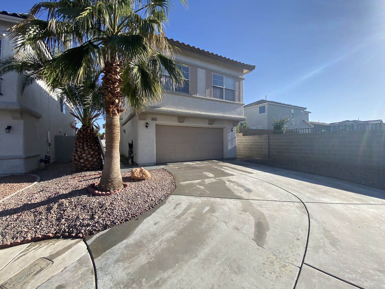Two-story home with clean concrete driveway and palm tree under blue sky