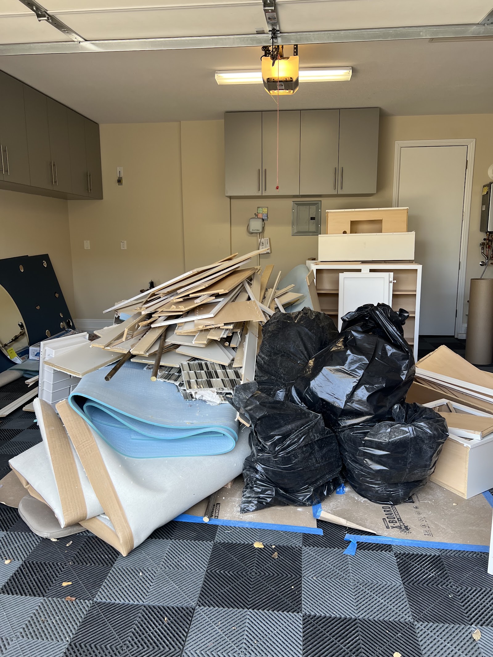 Garage filled with construction debris, wood scraps, carpet padding, and black trash bags ready for removal