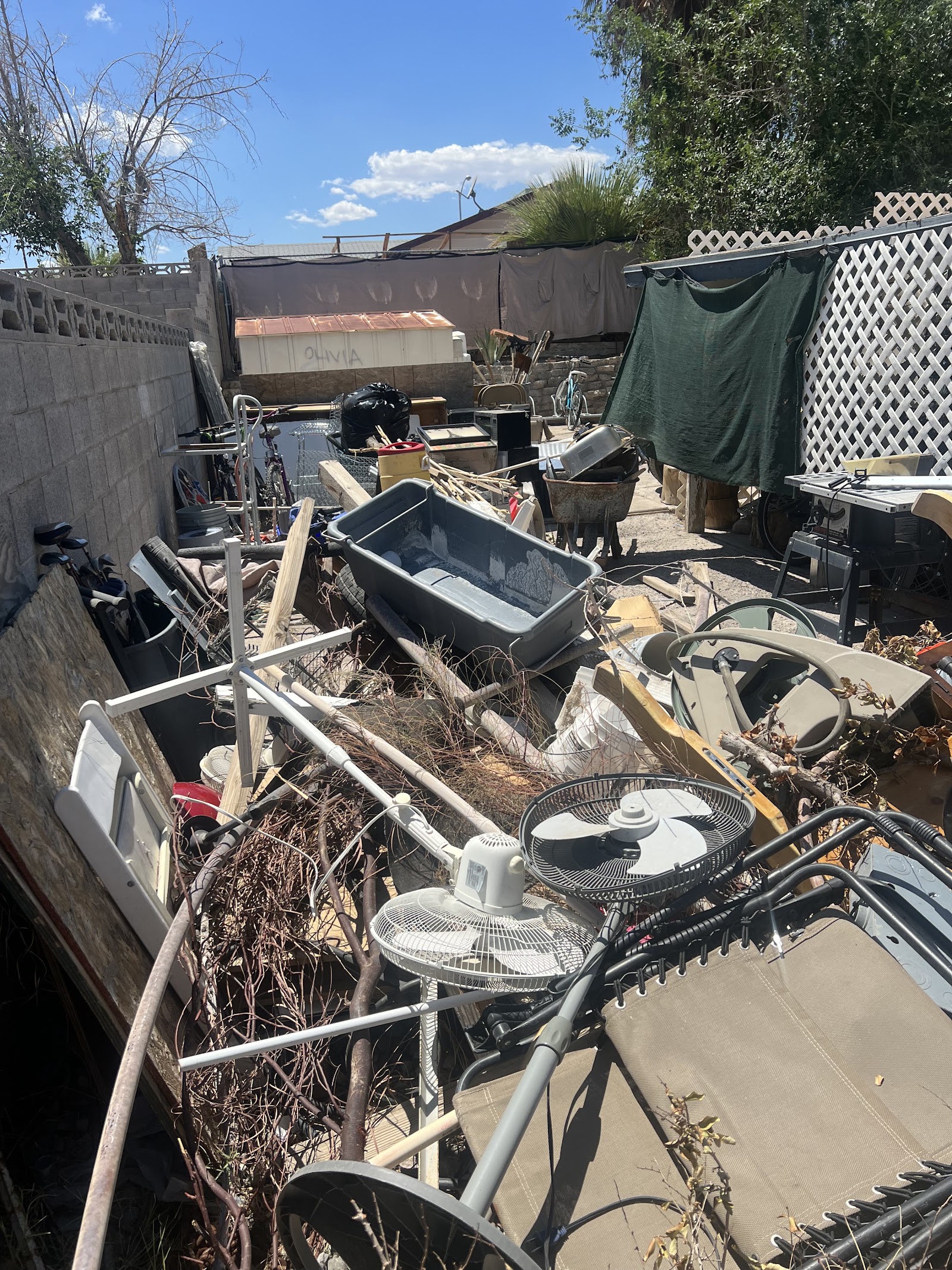 Cluttered backyard filled with junk including fans, furniture, bins, and yard debris