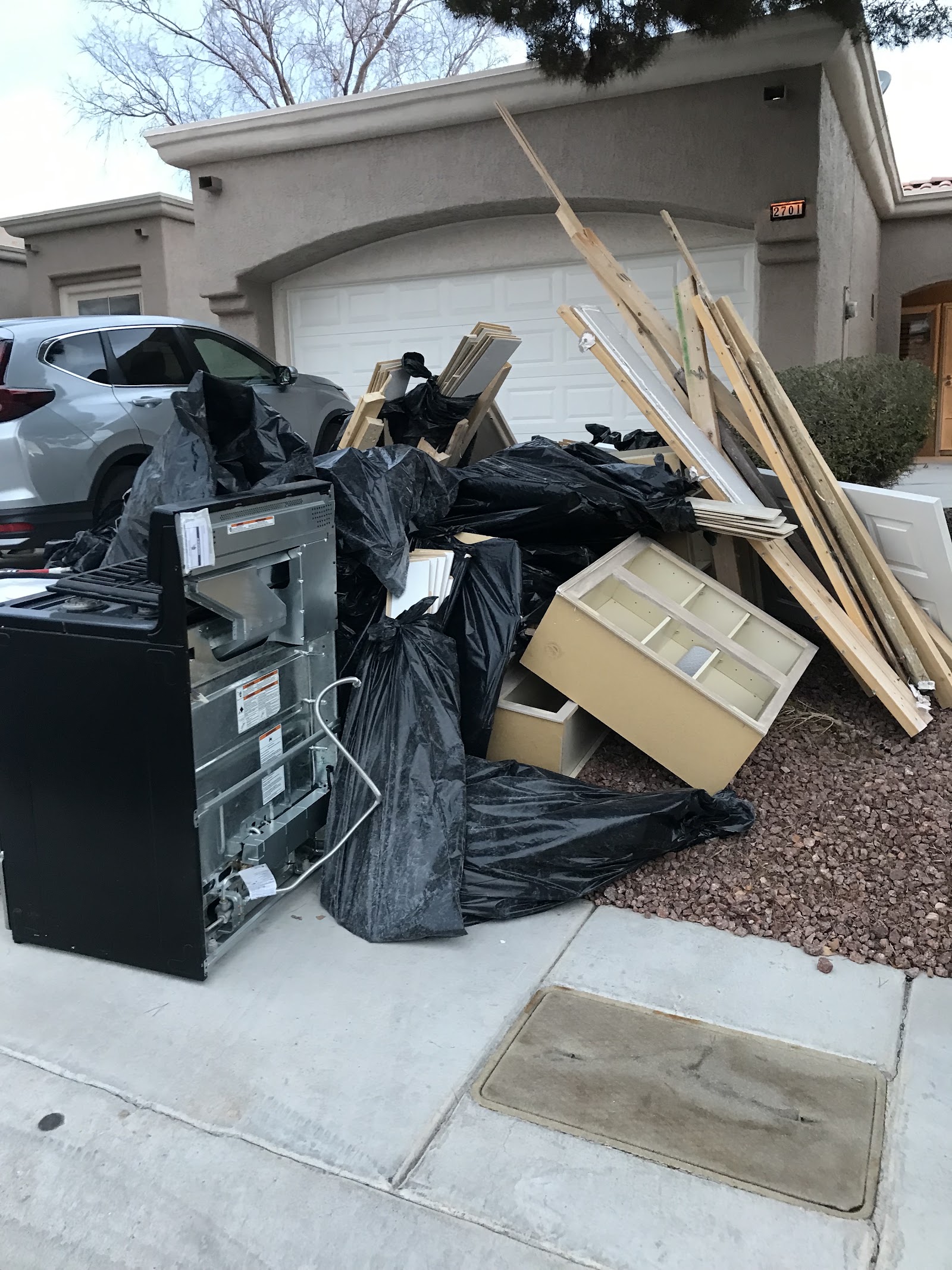 Curbside pile of appliances, trash bags, lumber, and cabinets staged for removal