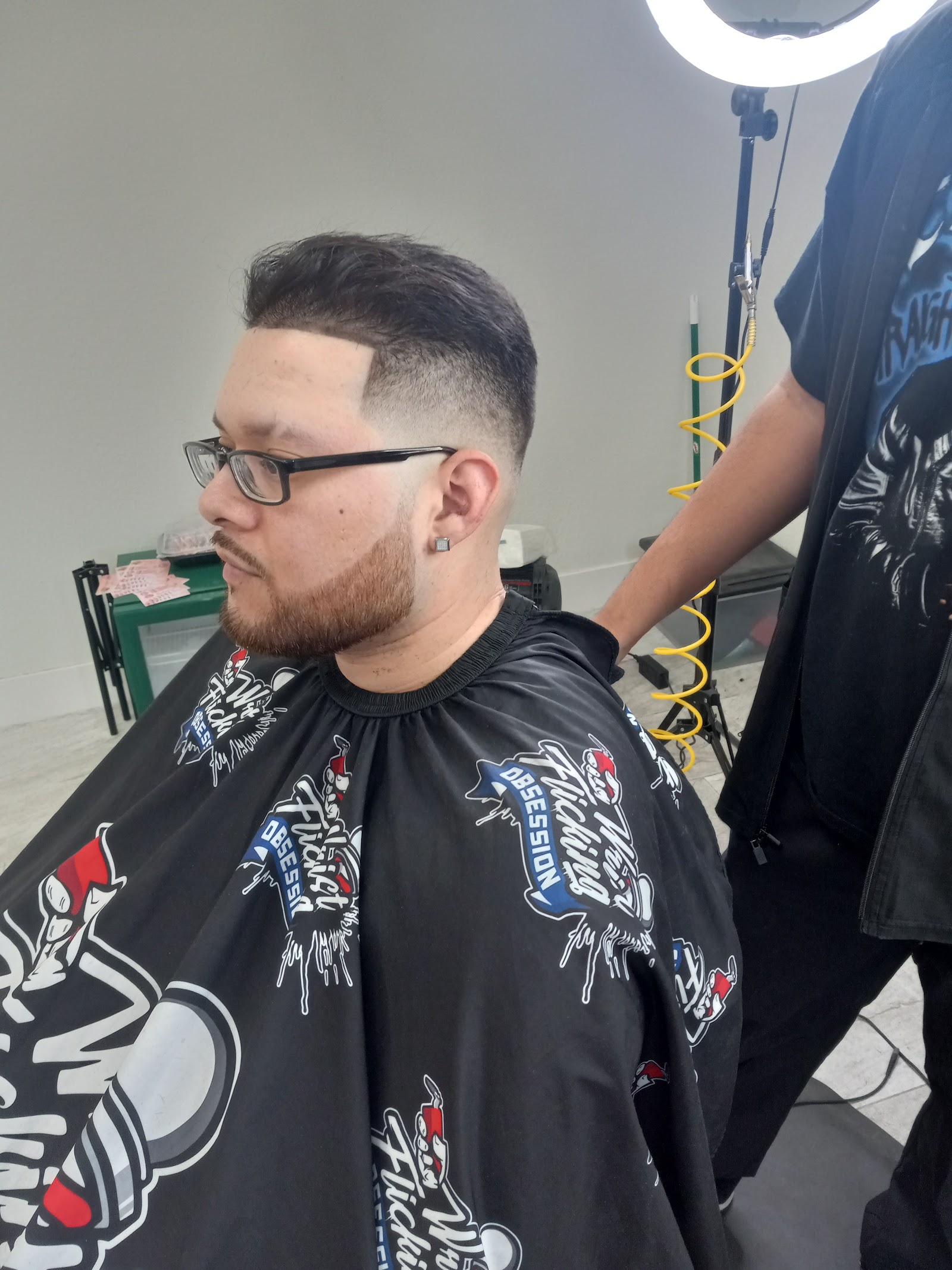 Man with fresh taper fade haircut wearing barber cape in shop