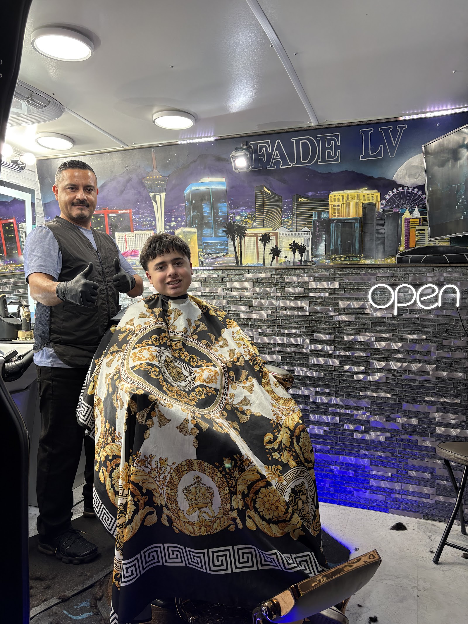 Barber giving thumbs up next to smiling young client caped up in the barbershop