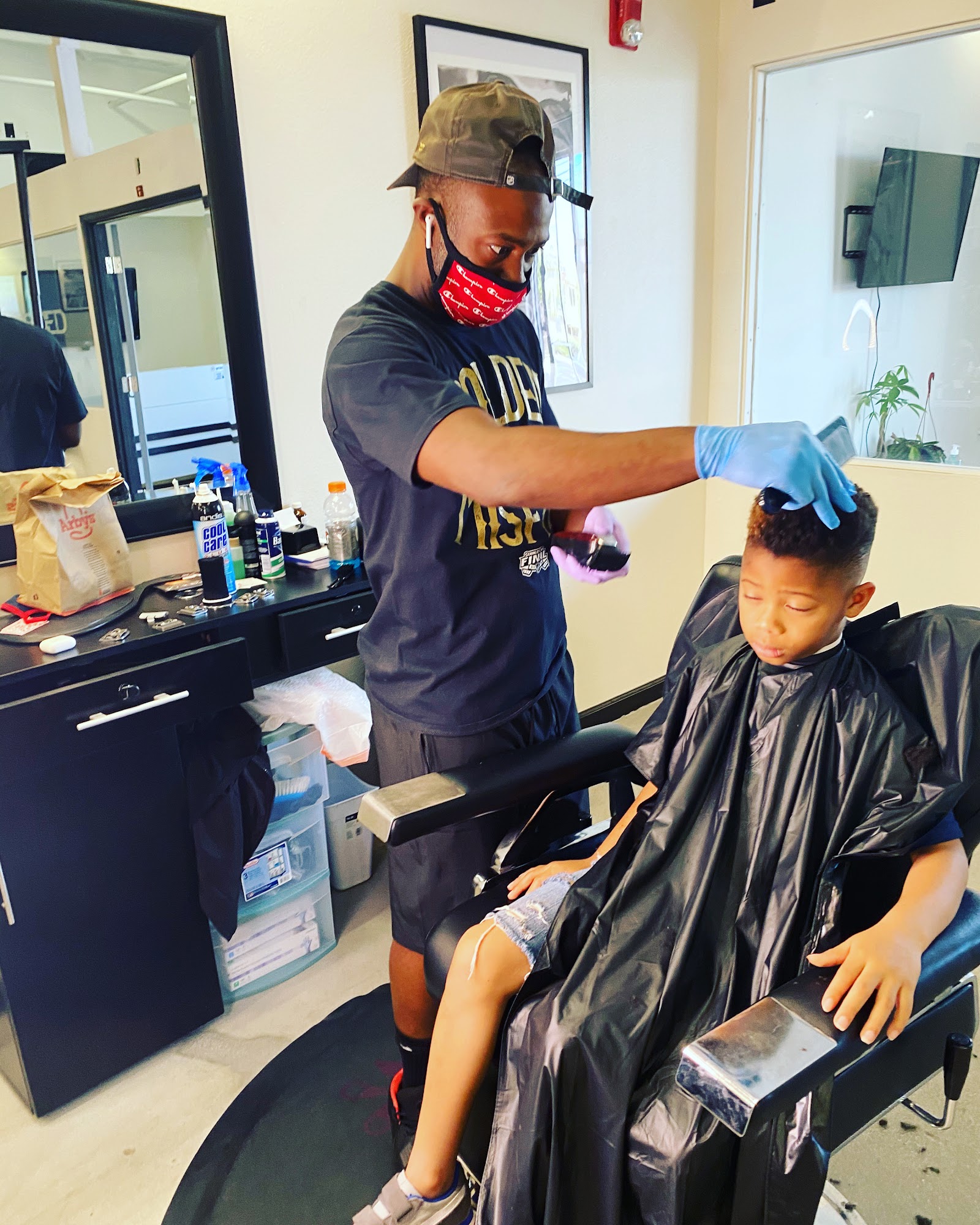 Barber in mask and gloves cutting a young boy's hair in the barbershop
