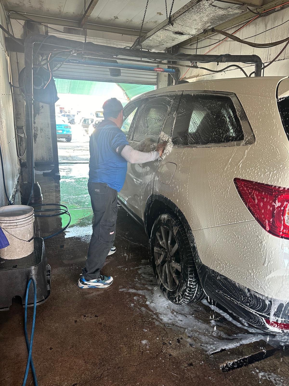 Worker hand washing a soapy white SUV inside a wash bay