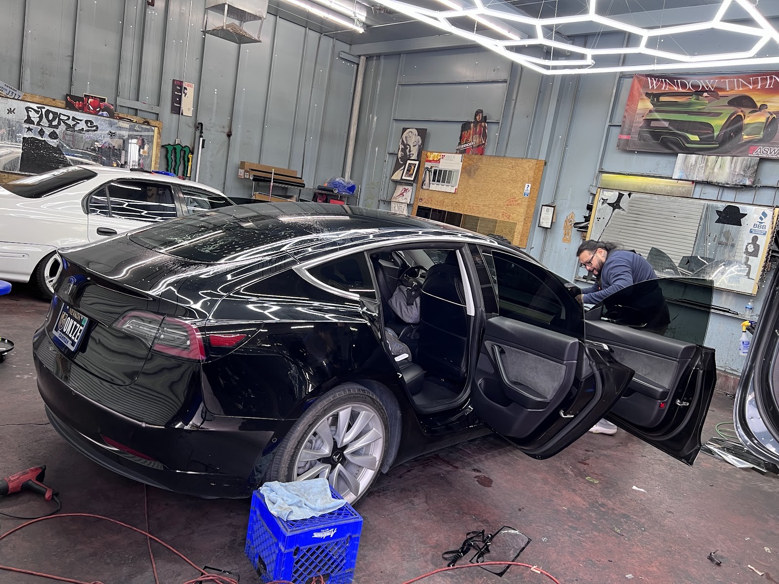 Black Tesla Model 3 with doors open during window tinting inside the shop