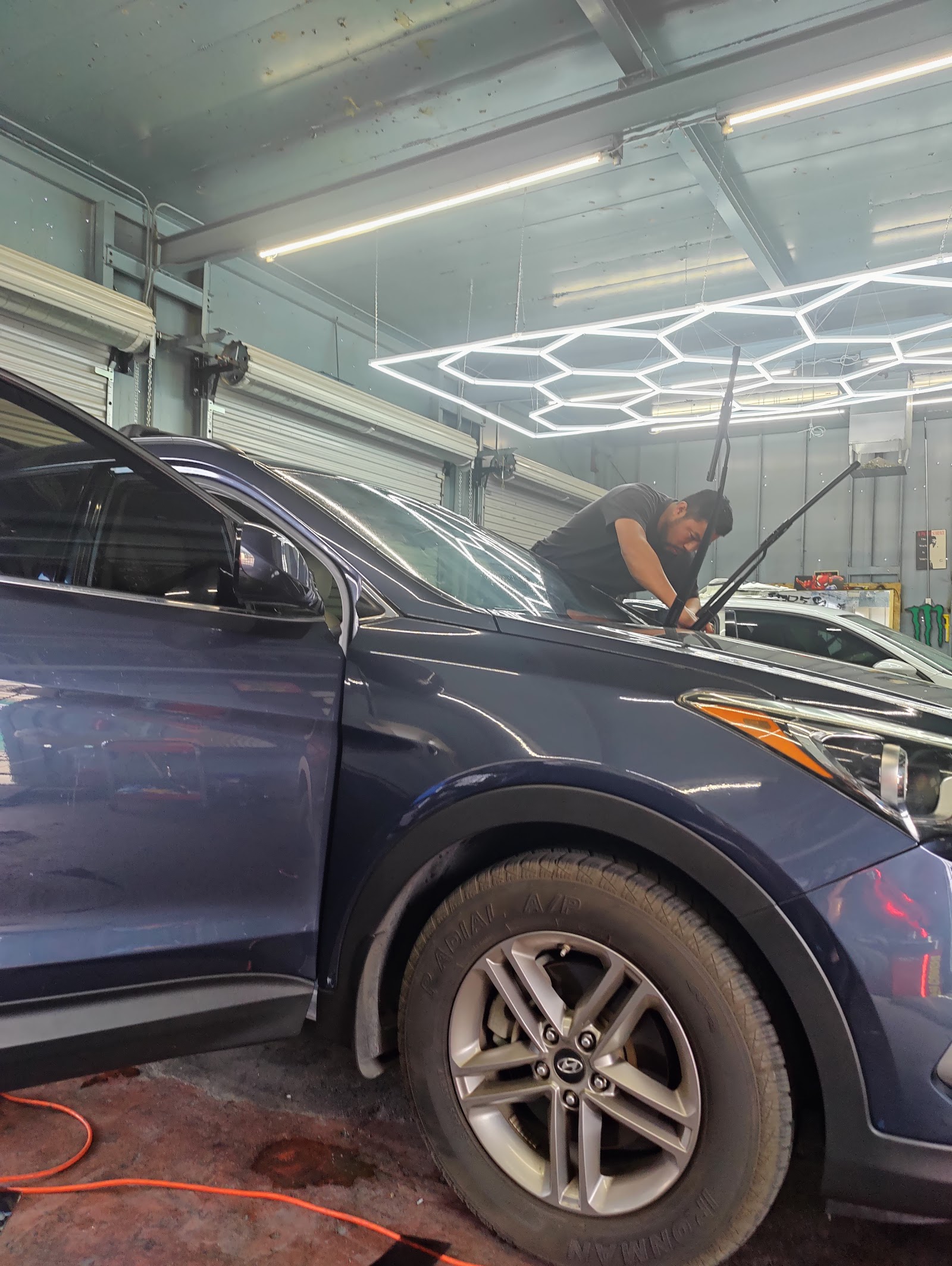 Technician installing window tint on windshield of a blue Hyundai SUV inside shop