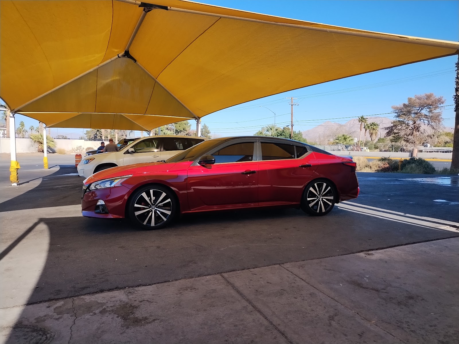 Red Nissan Altima parked under yellow shade canopy at car wash