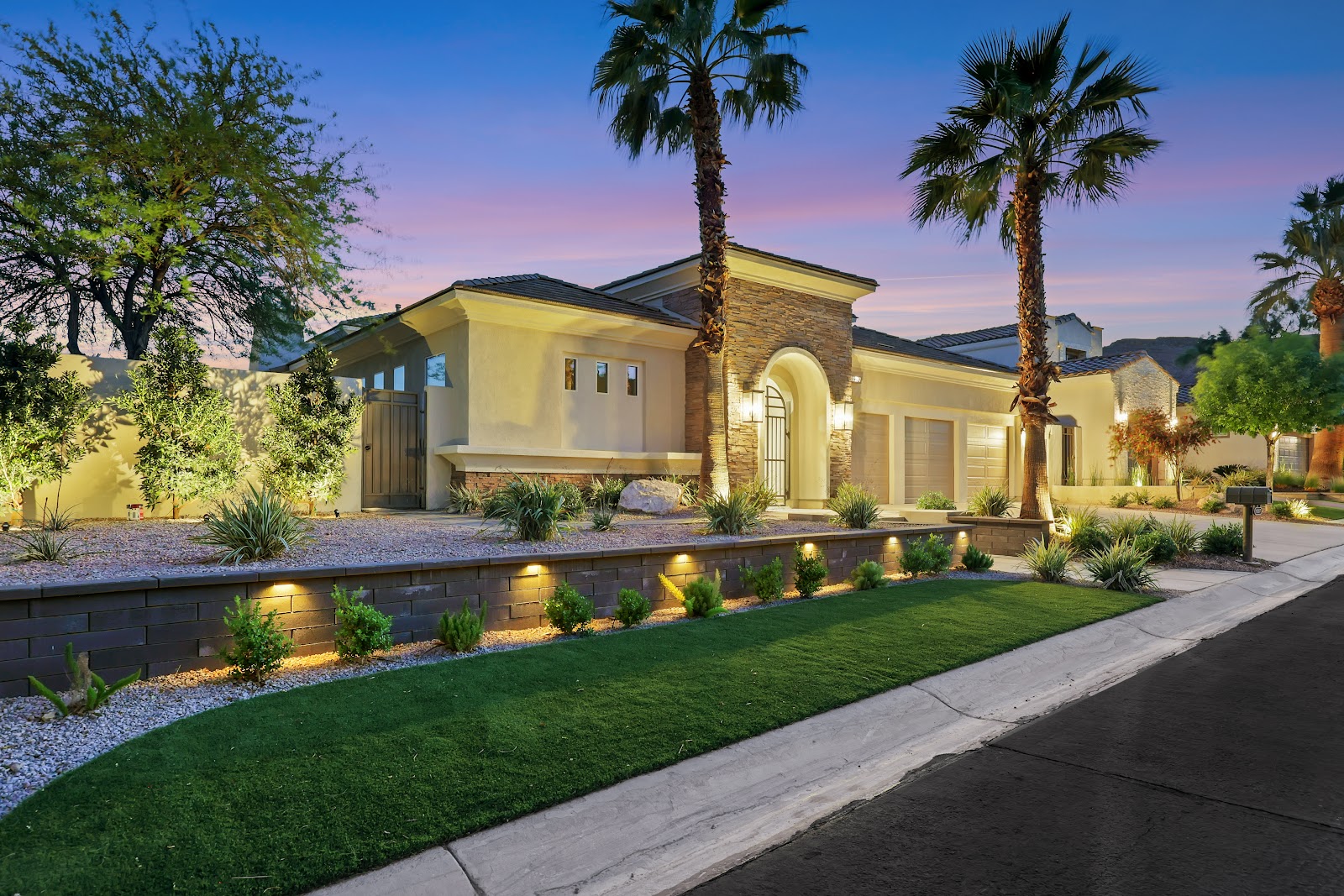 Luxury home at dusk with landscape lighting, turf lawn and retaining wall