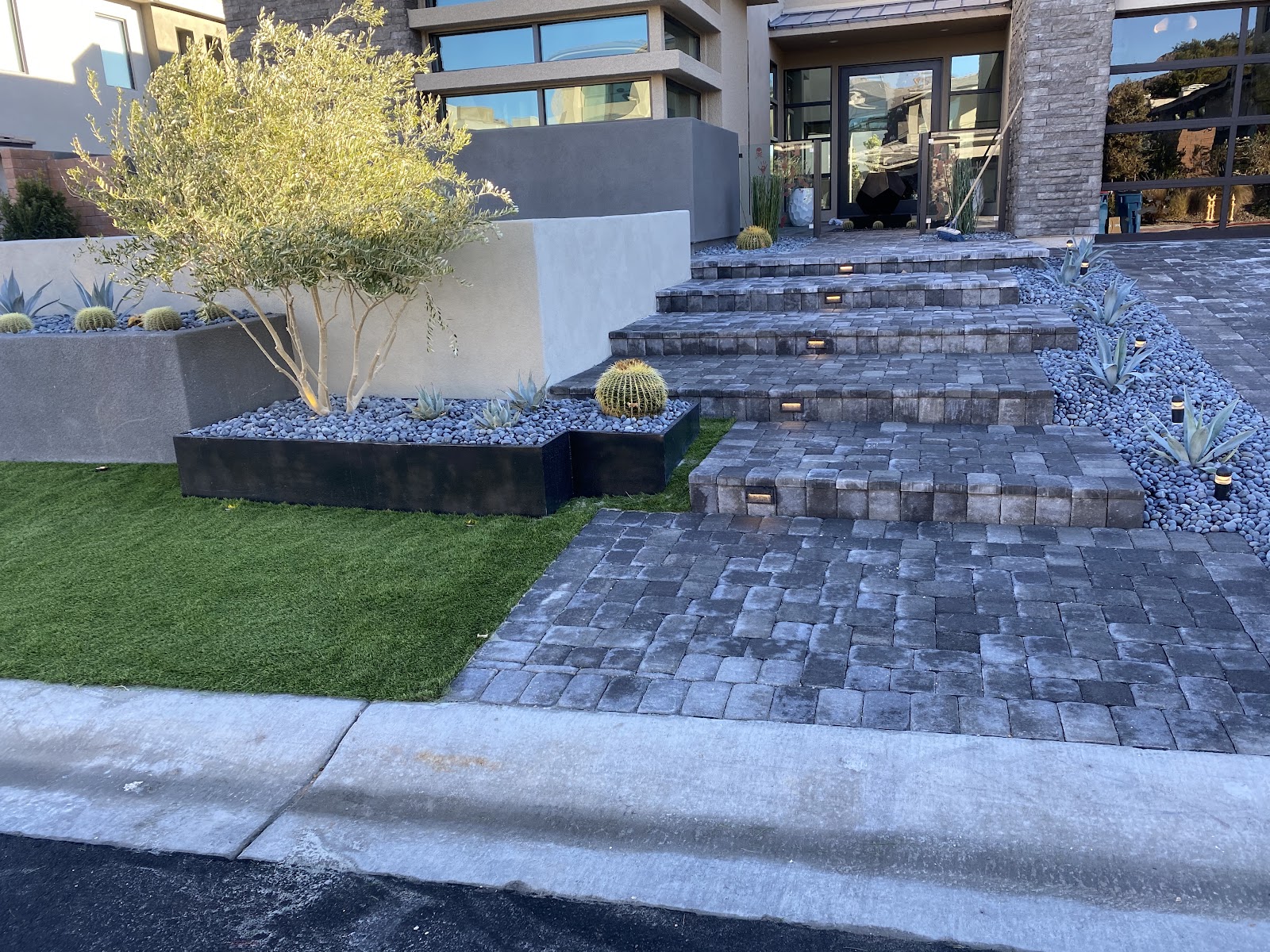 Modern home entrance with paver steps, turf lawn and cactus planters