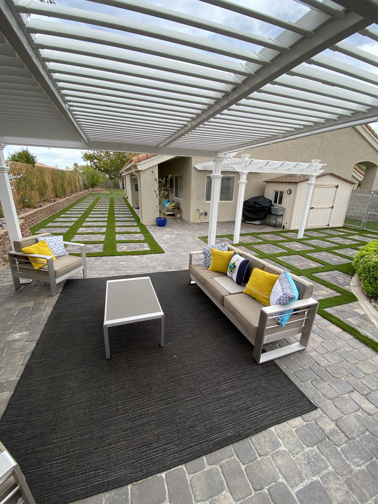 Covered patio with pergola, paver flooring and turf-and-paver checkerboard yard