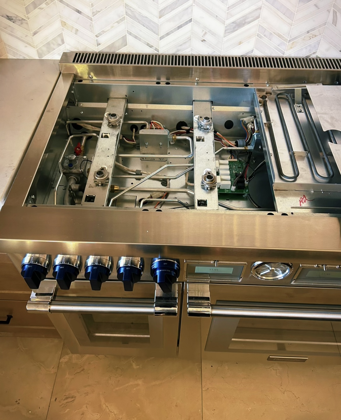 Professional stainless gas range with top removed exposing burners and control board during repair