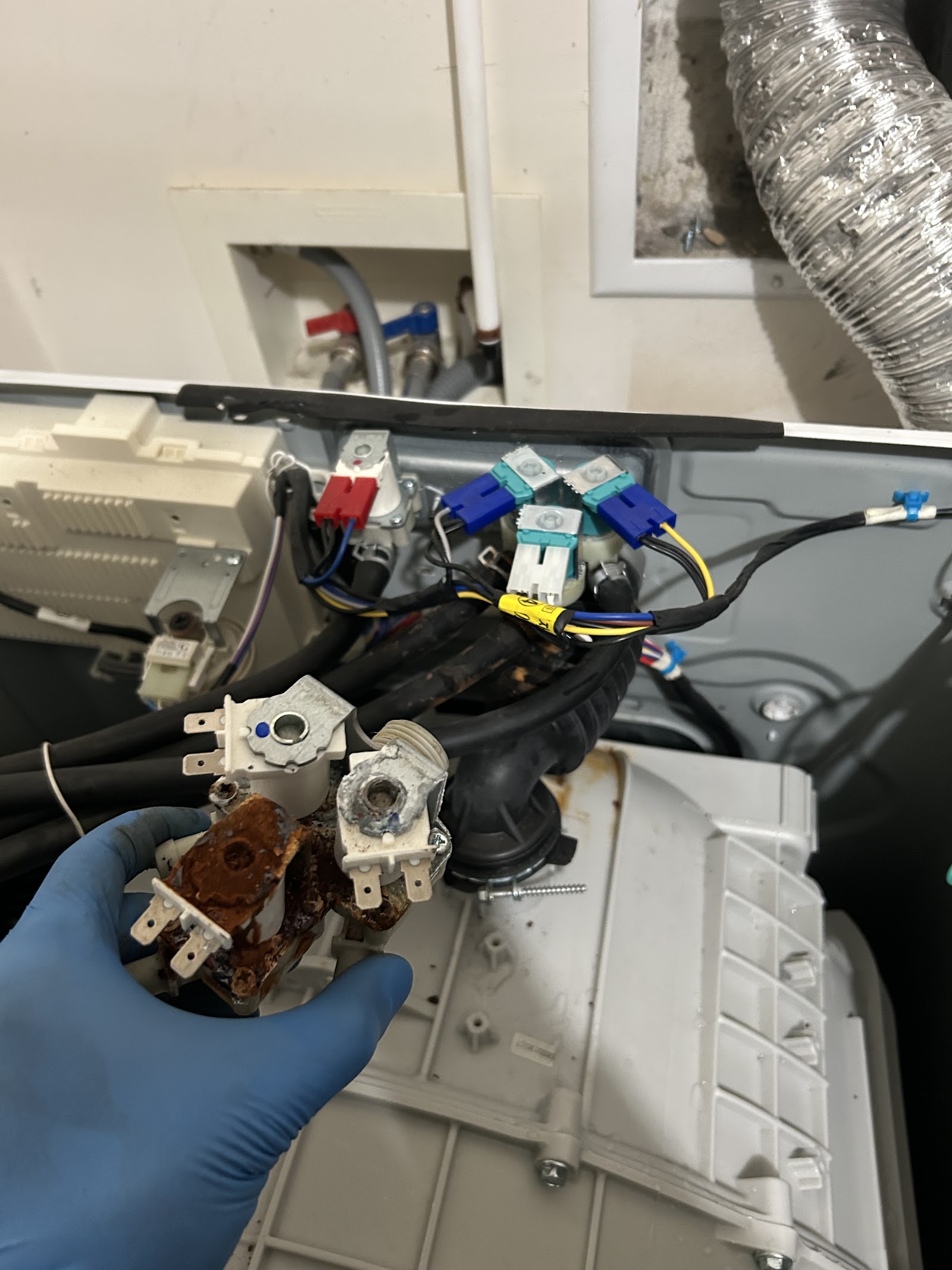 Gloved hand holding heavily rusted water inlet valve removed from washer