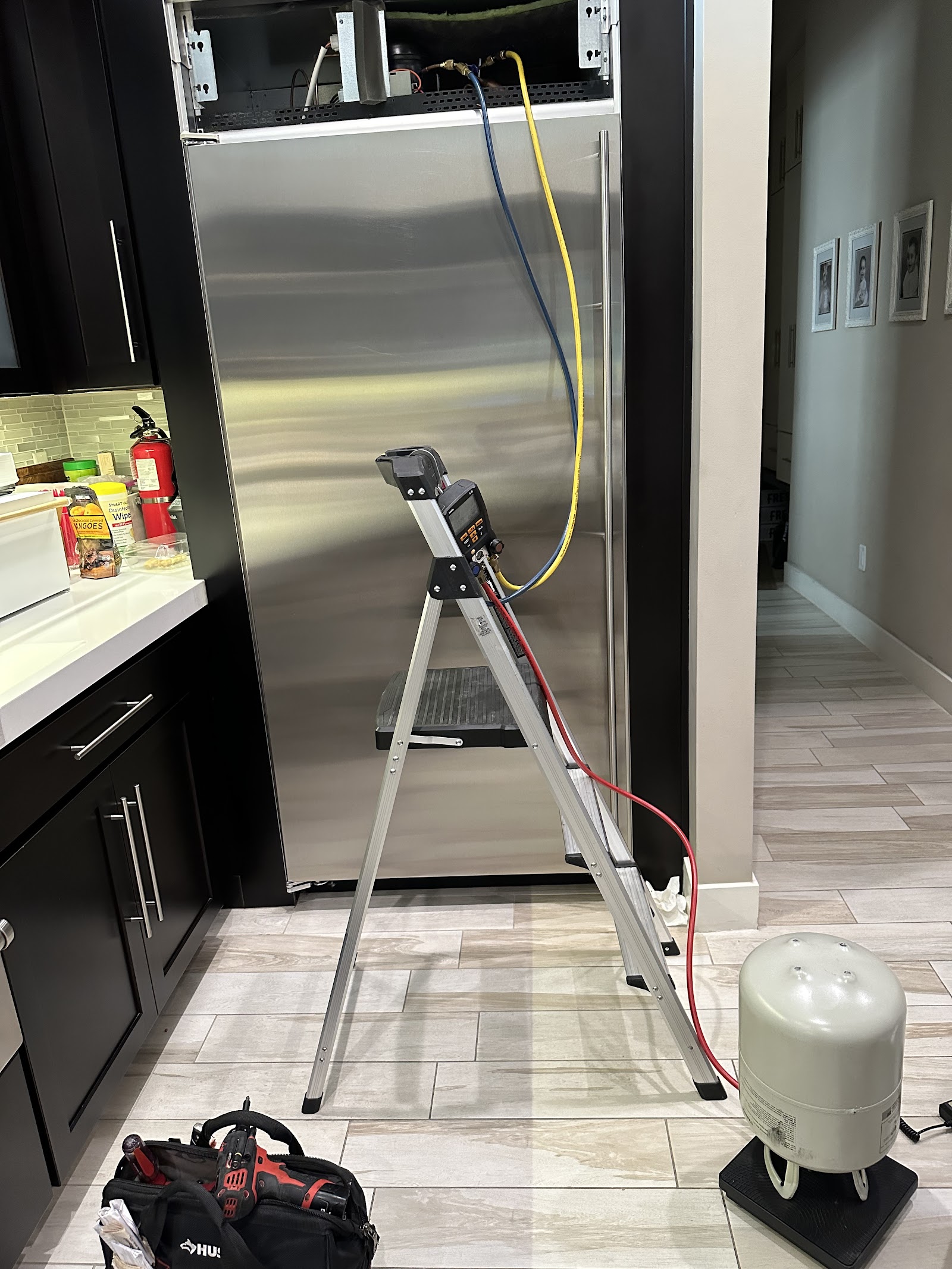 Built-in stainless refrigerator being serviced with refrigerant gauges and recovery tank