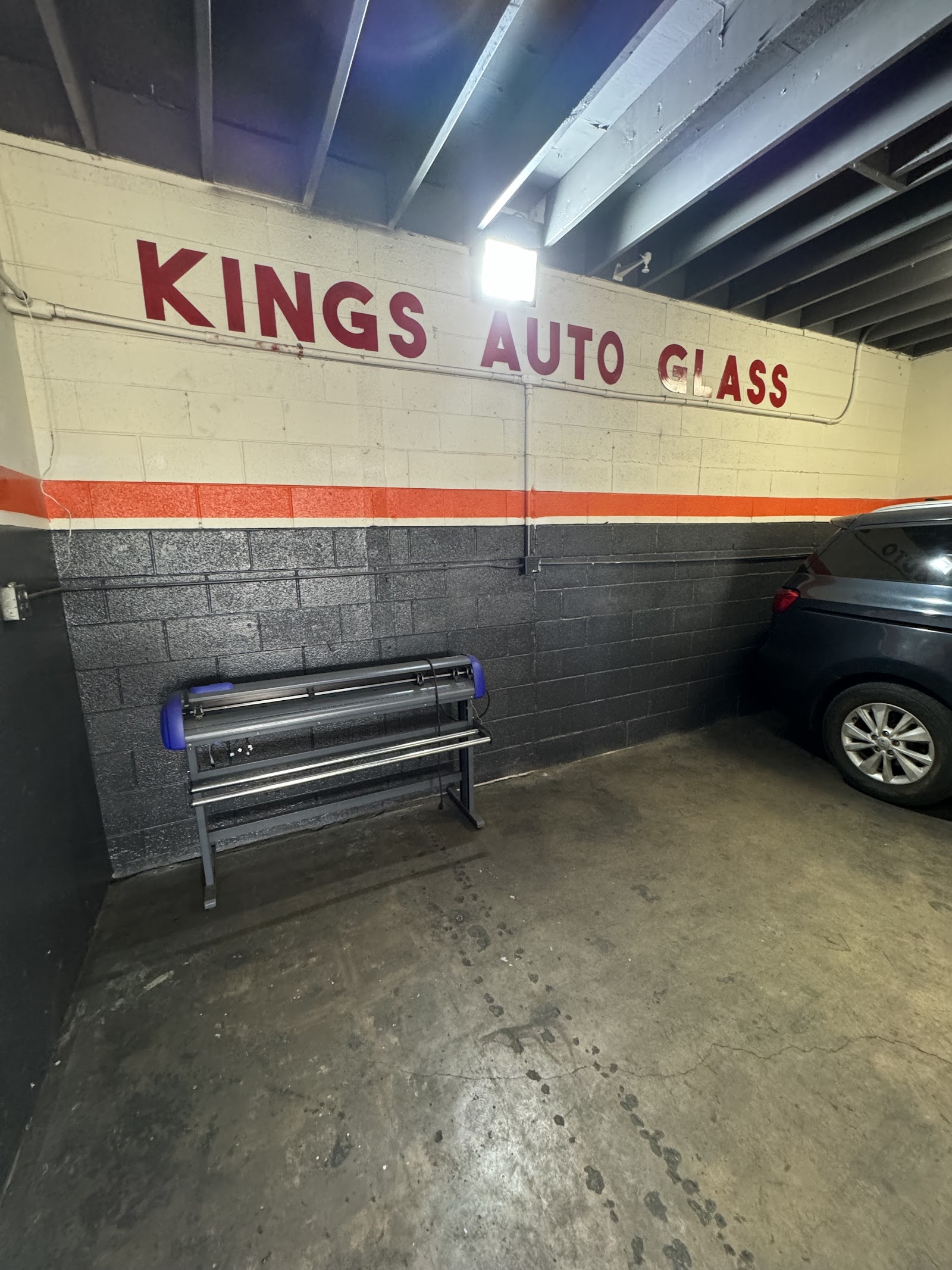 Interior garage bay with 'Kings Auto Glass' painted wall and window tint film cutting machine