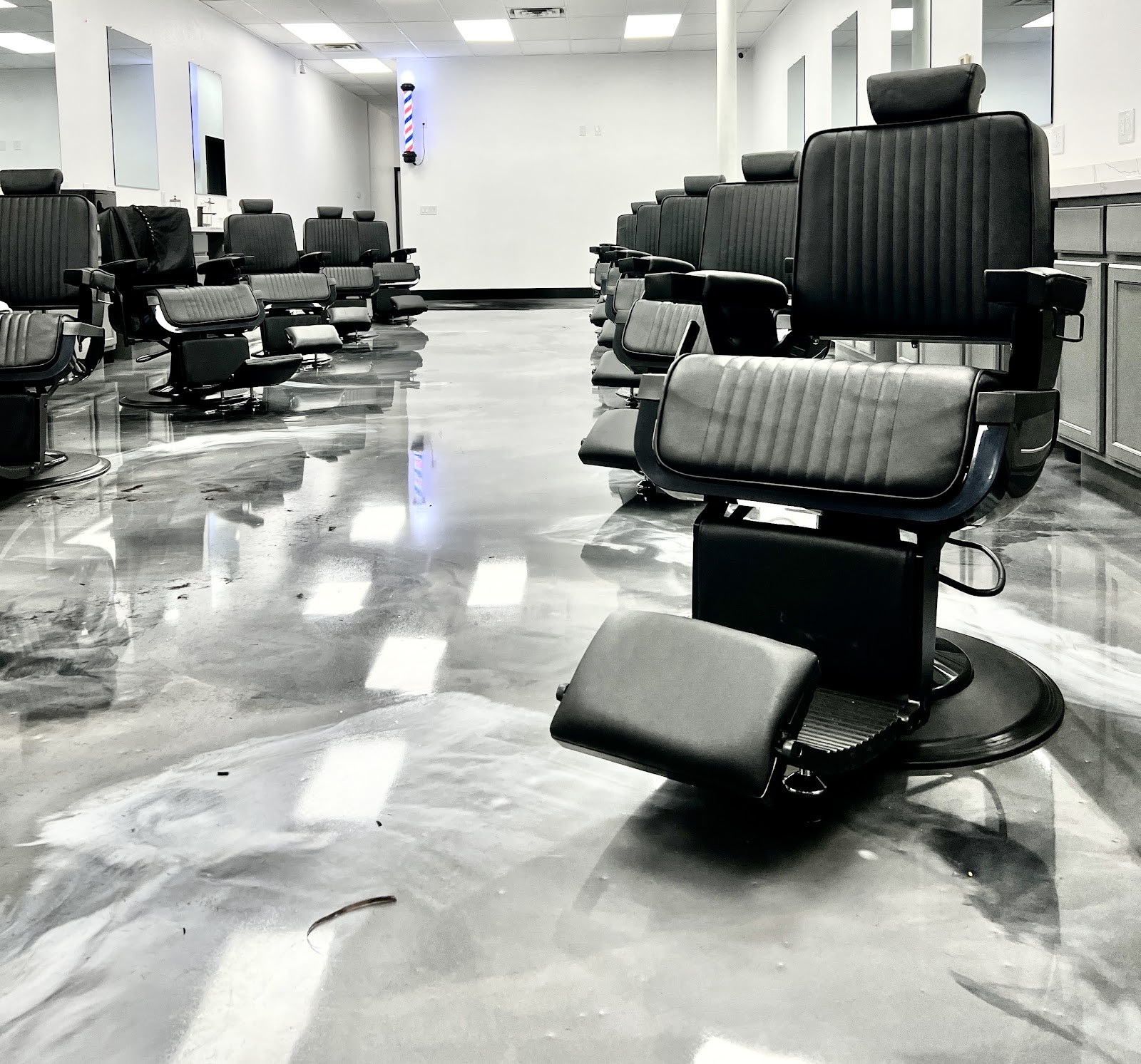 Black barber chairs and glossy silver epoxy floor with barber pole in background