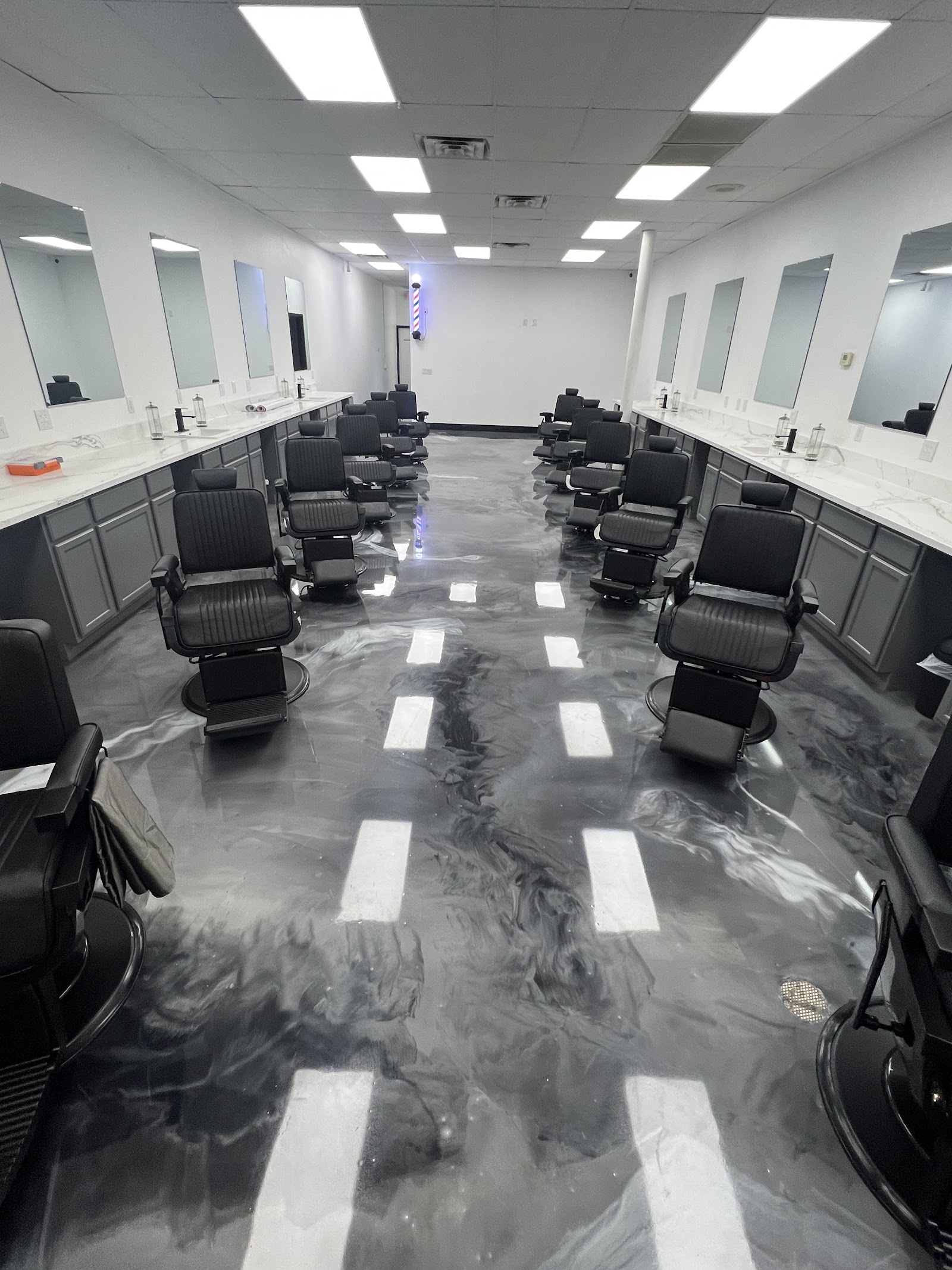 Rows of black barber chairs facing mirrors with marble-effect epoxy floor