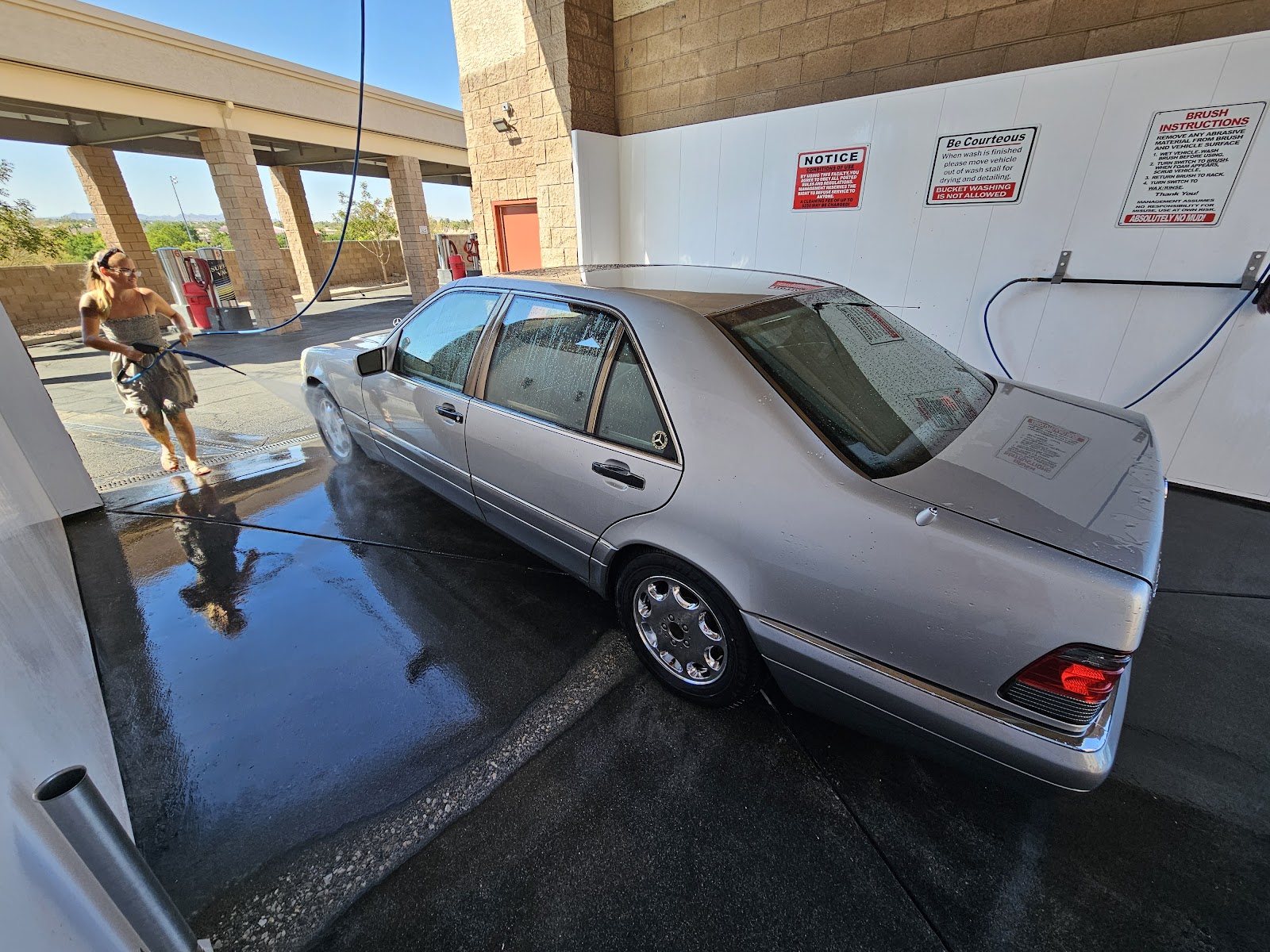 Person washing a silver Mercedes-Benz S-Class sedan at self-serve wash bay