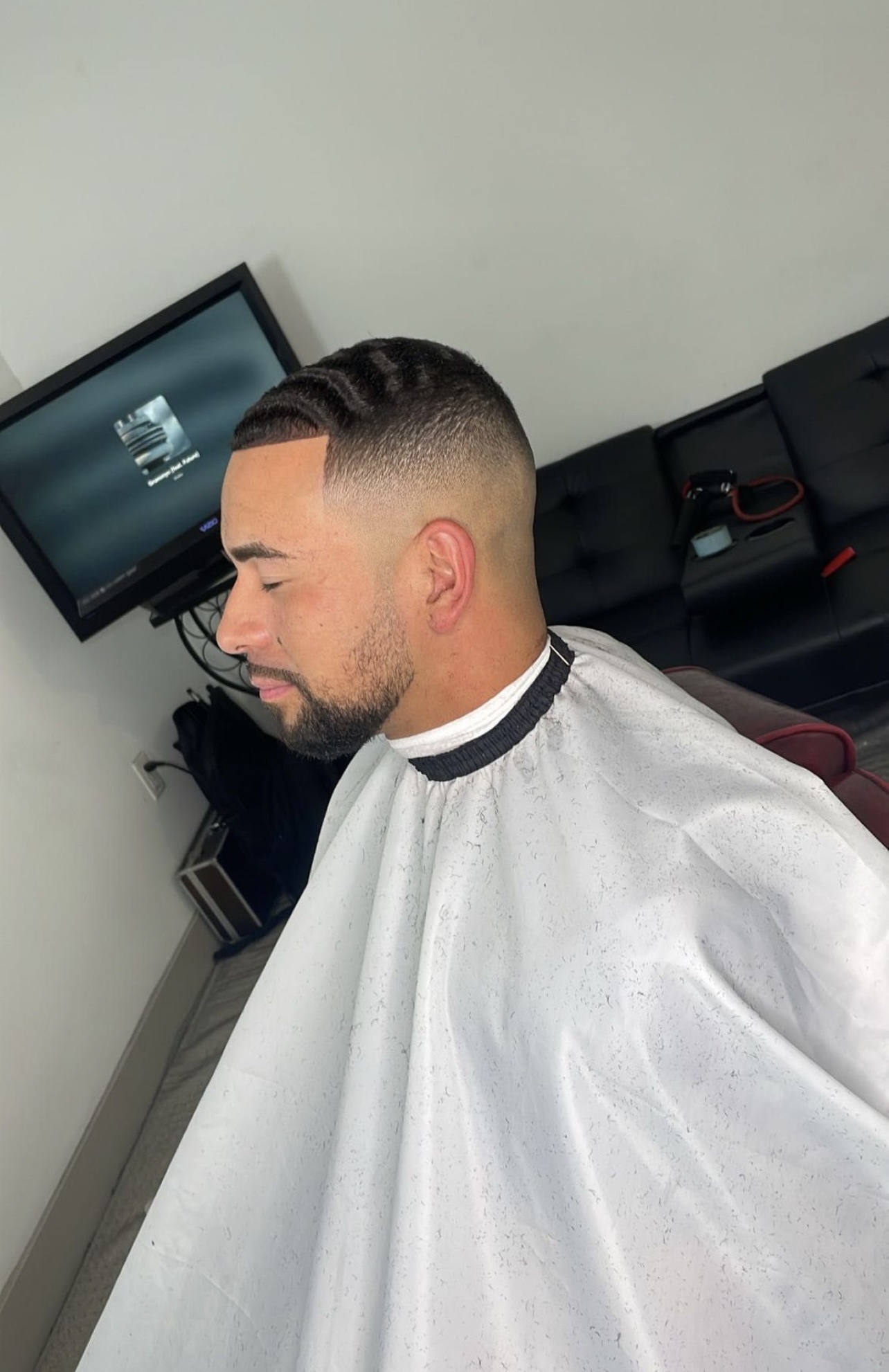 Man with clean fade haircut, waves, and lineup wearing white barber cape